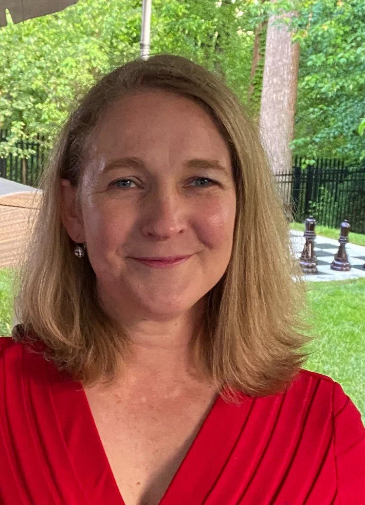 Smiling woman with long, straight hair with a green park background.