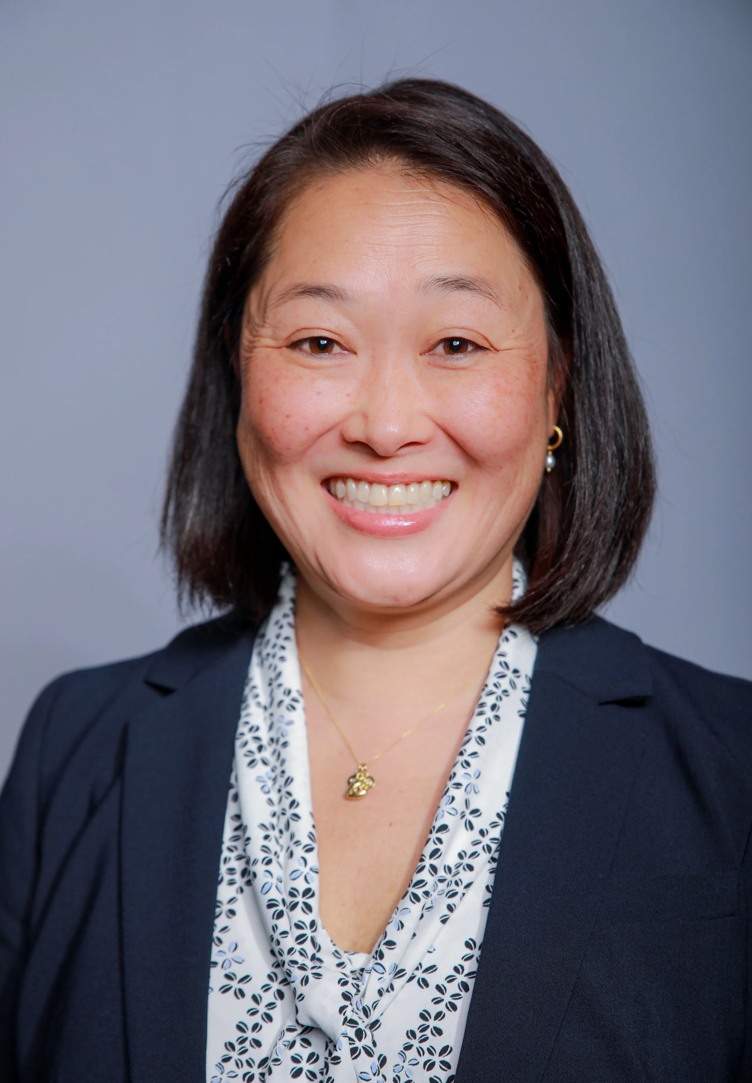 Smiling woman with short, straight hair on a medium gray background.