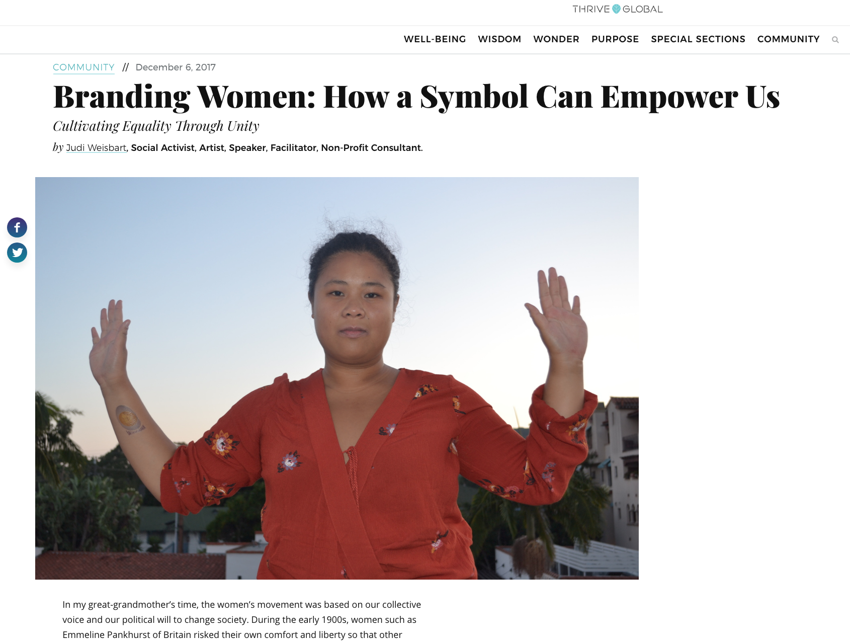 A woman wearing a red blouse with floral embroidery holds her arms up with palms facing outward, standing outdoors during sunset with buildings and palm trees in the background.