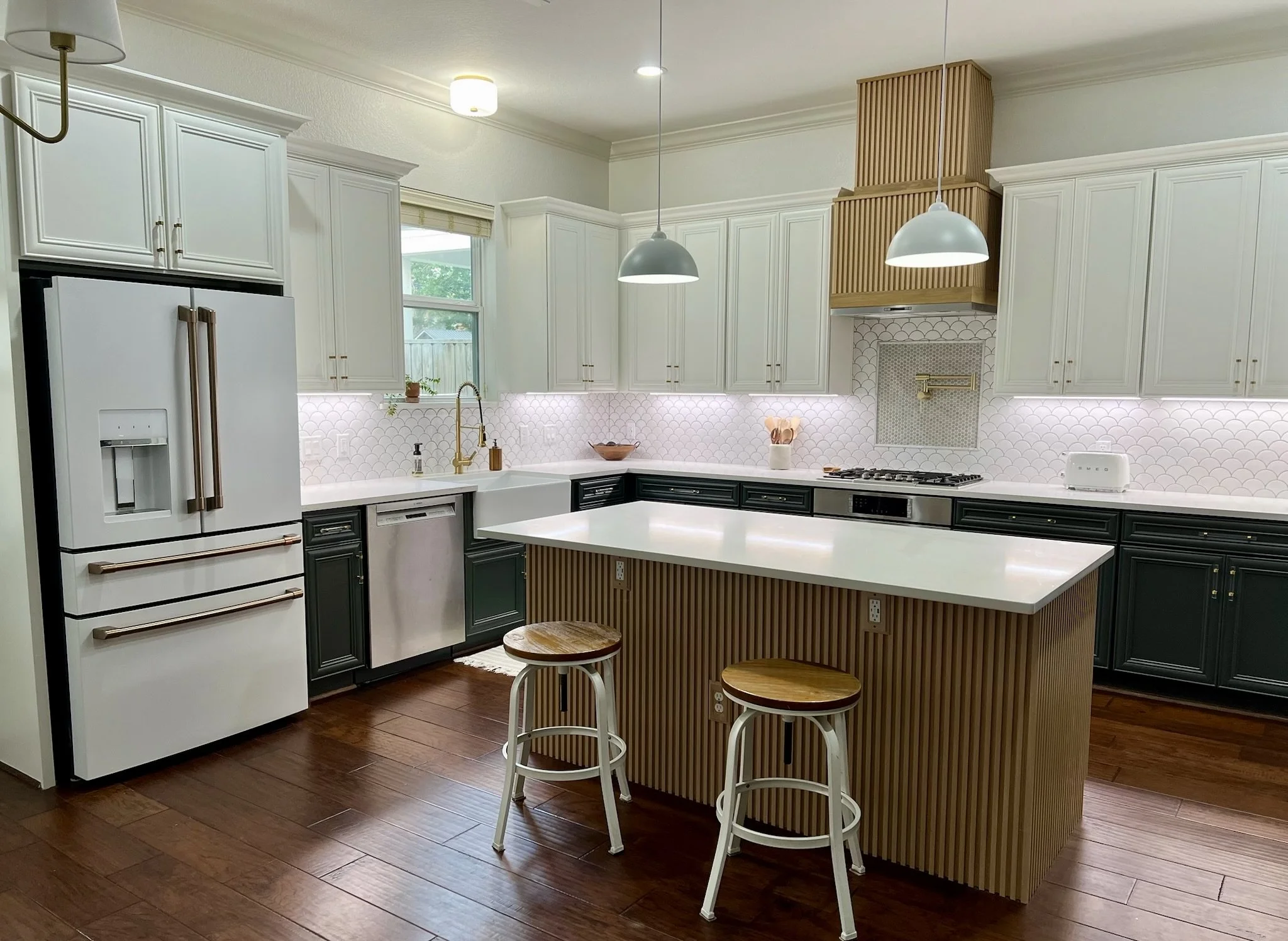 Kitchen remodel with white quartz countertops & island, pendant lighting & flush-mount sink lighting installation, fluted oak island and fluted oak range hood. Updated ceramic backsplash with stone & marble tile accent to house install of pot filler