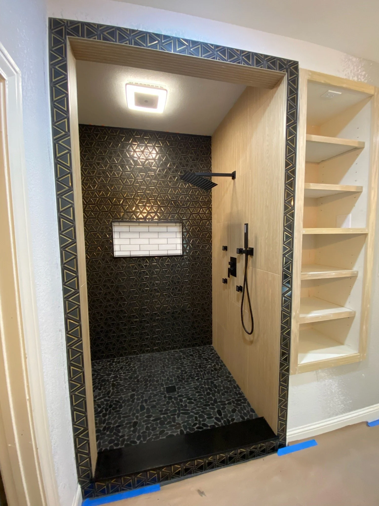 Primary shower expansion with black & gold stone & glass tile, wood-look tile, stone shower floor tile, tiled frame & install of secondary linen closet.