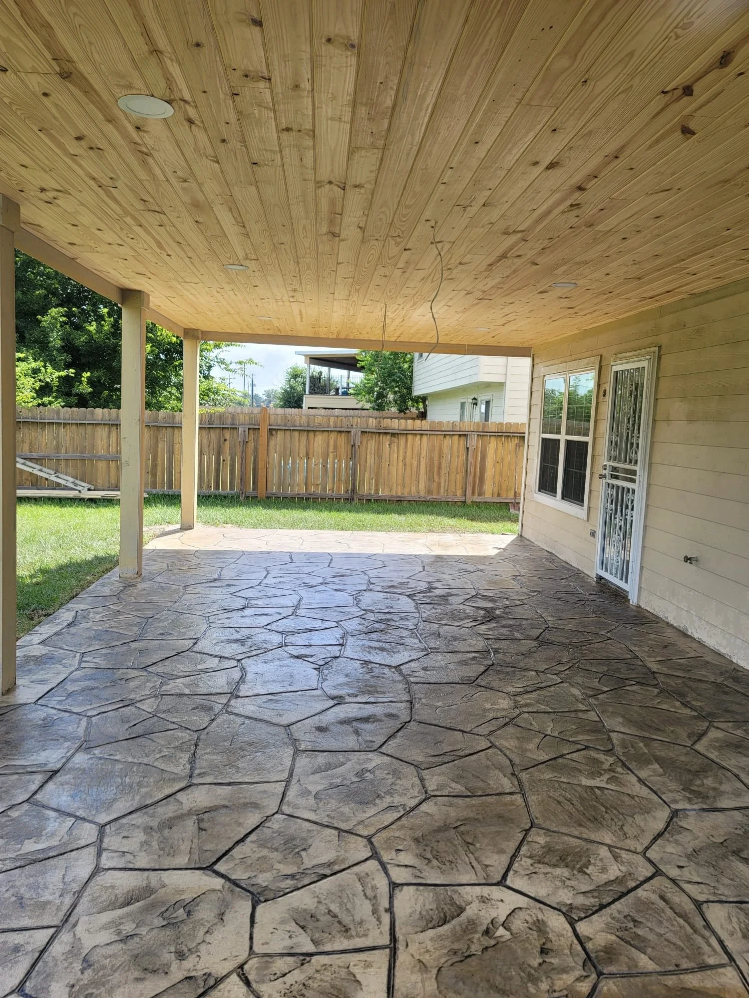 Covered outdoor patio with natural stained wood ceiling & stone patio. Wood columns.
