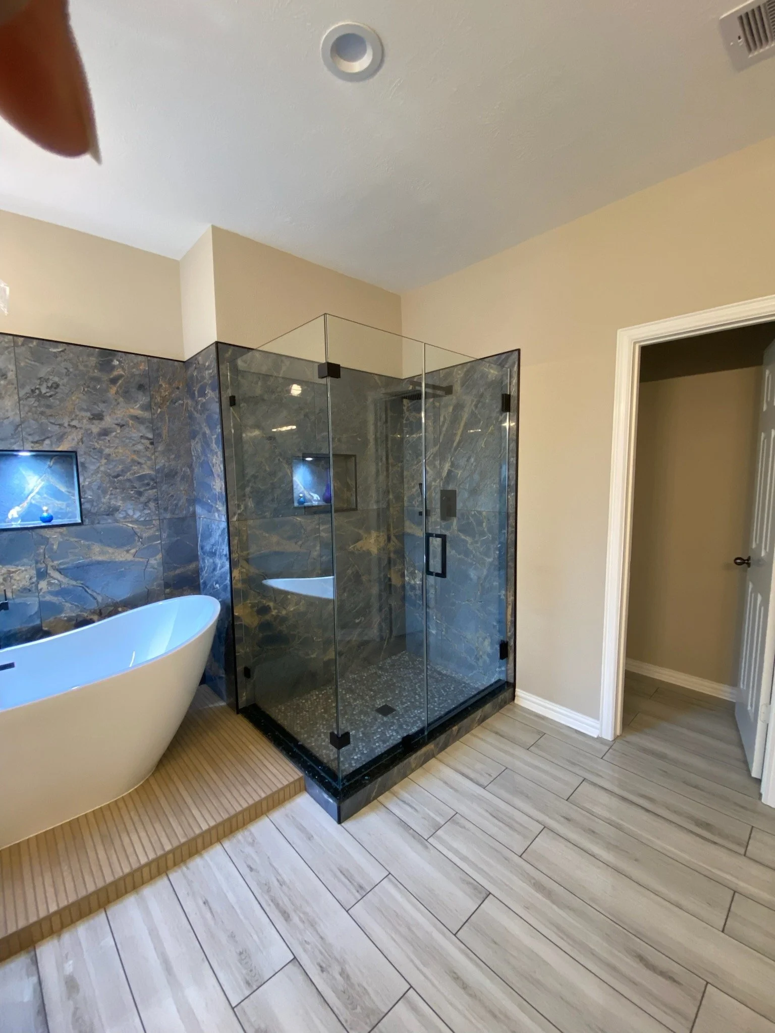 Primary bathroom update with new tub & custom tiled platform, wood-look tile flooring, stone tile & custom created seamless shower glass.