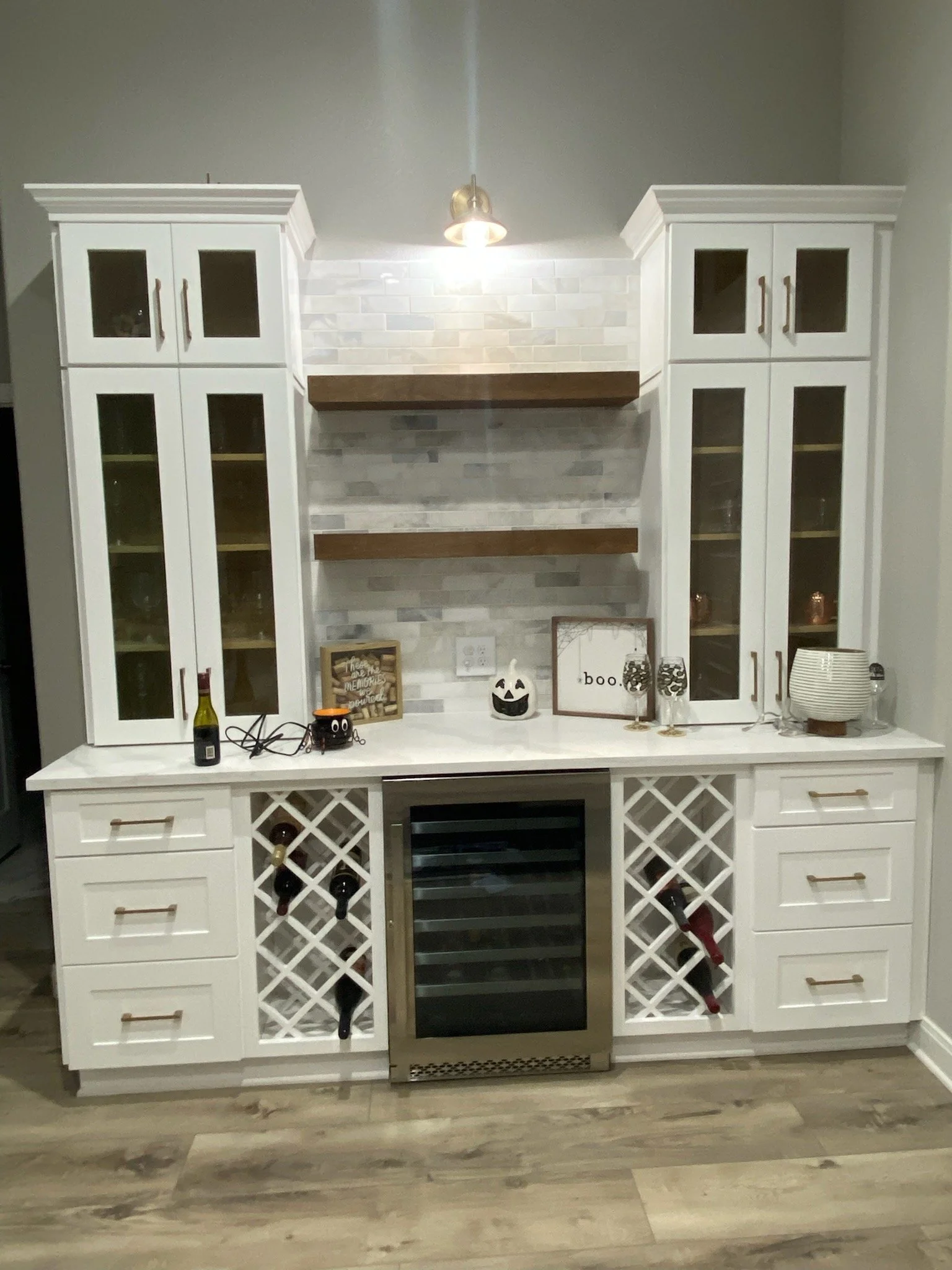 Custom built open wet bar with wine storage, glass-front cabinetry and drawers for storage. Stone accent wall, wooden floating shelving and lighting installed.