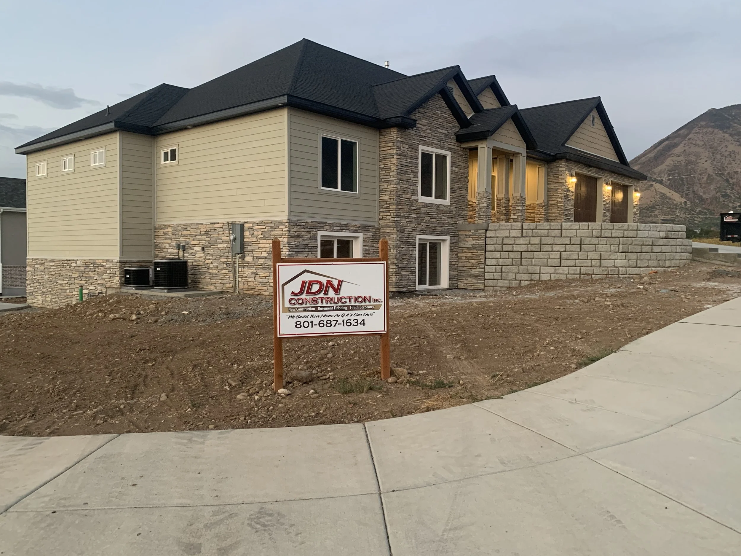 Newly constructed house with stone and siding exterior, lit windows, and a sign for JDN Construction in front, with a mountain in the background.
