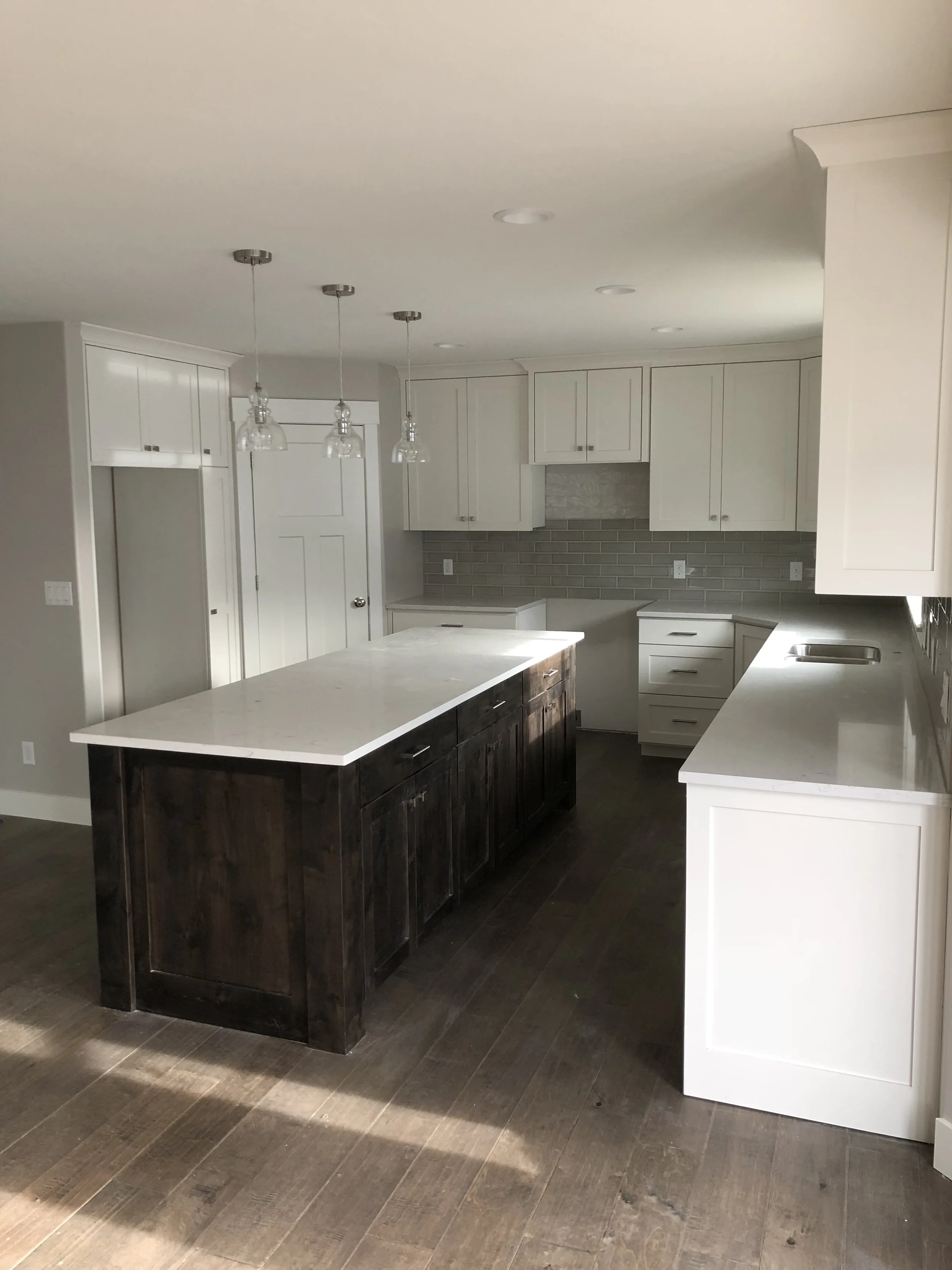 Modern kitchen with white cabinets, a central island with dark wood finish, white countertops, a gray brick backsplash, and pendant lighting.