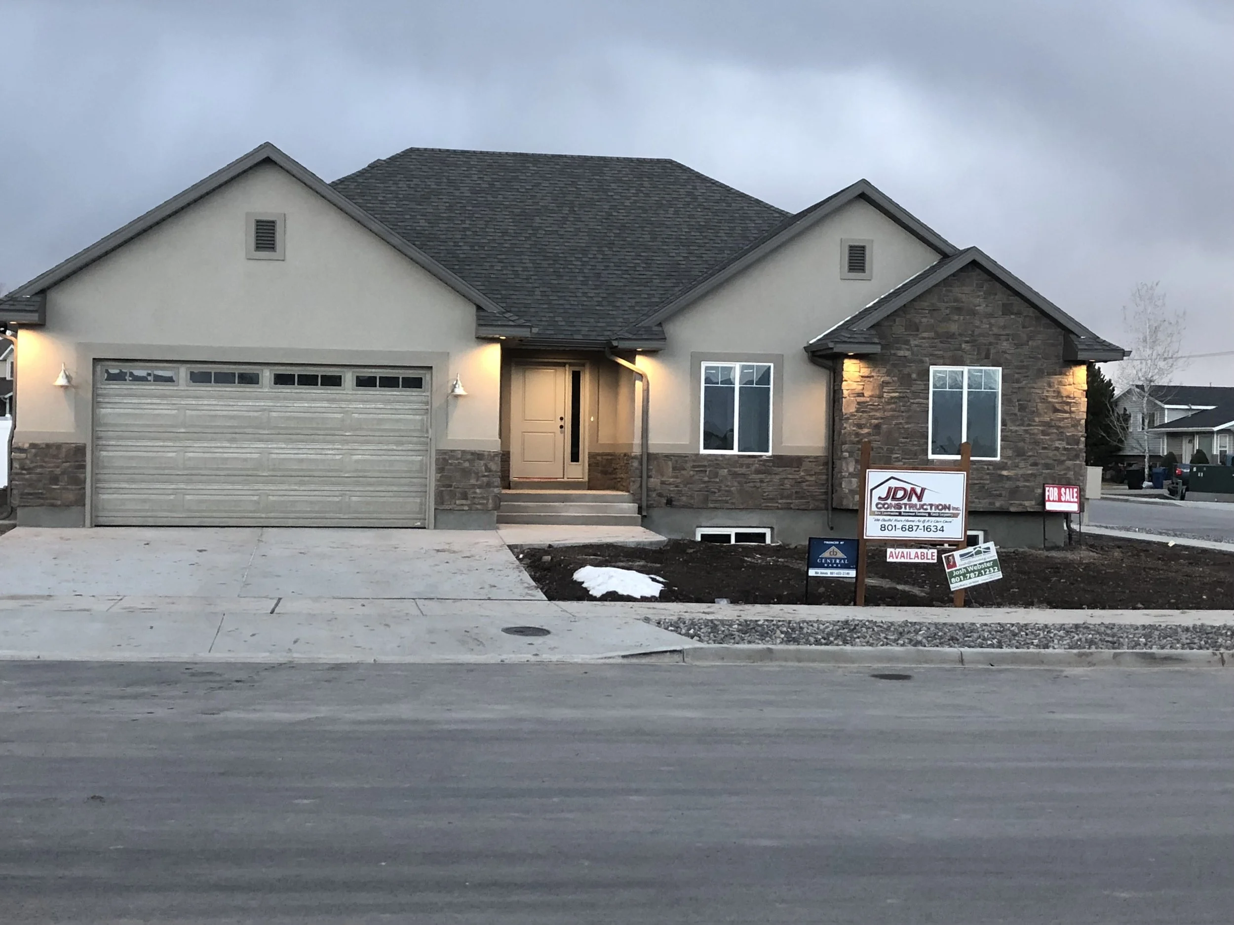 Newly constructed house with a two-car garage, front yard with construction signs, and a paved driveway.