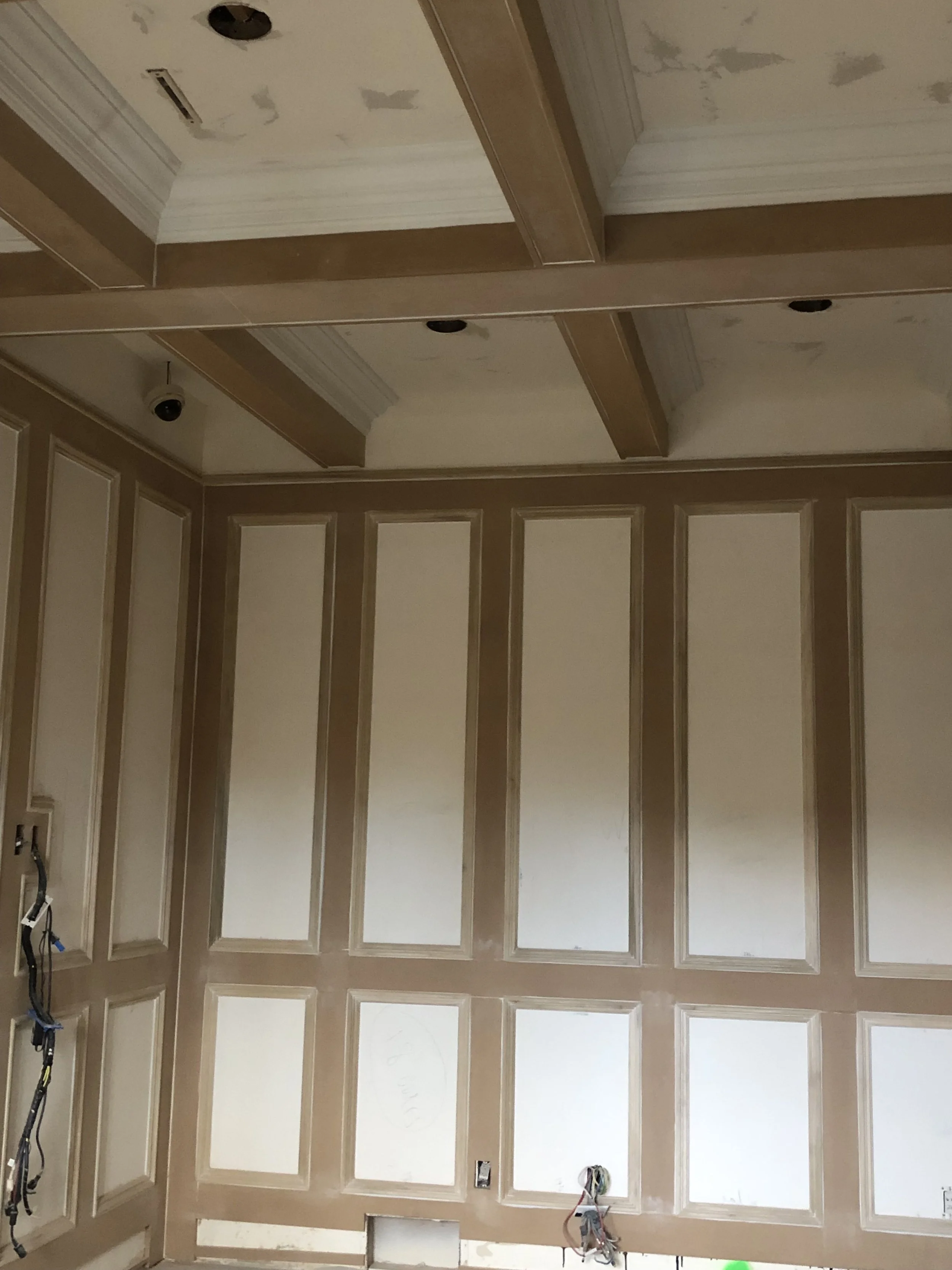 Interior of a room under renovation with beige paneled walls, a ceiling with crown molding, and exposed electrical wiring near the bottom.