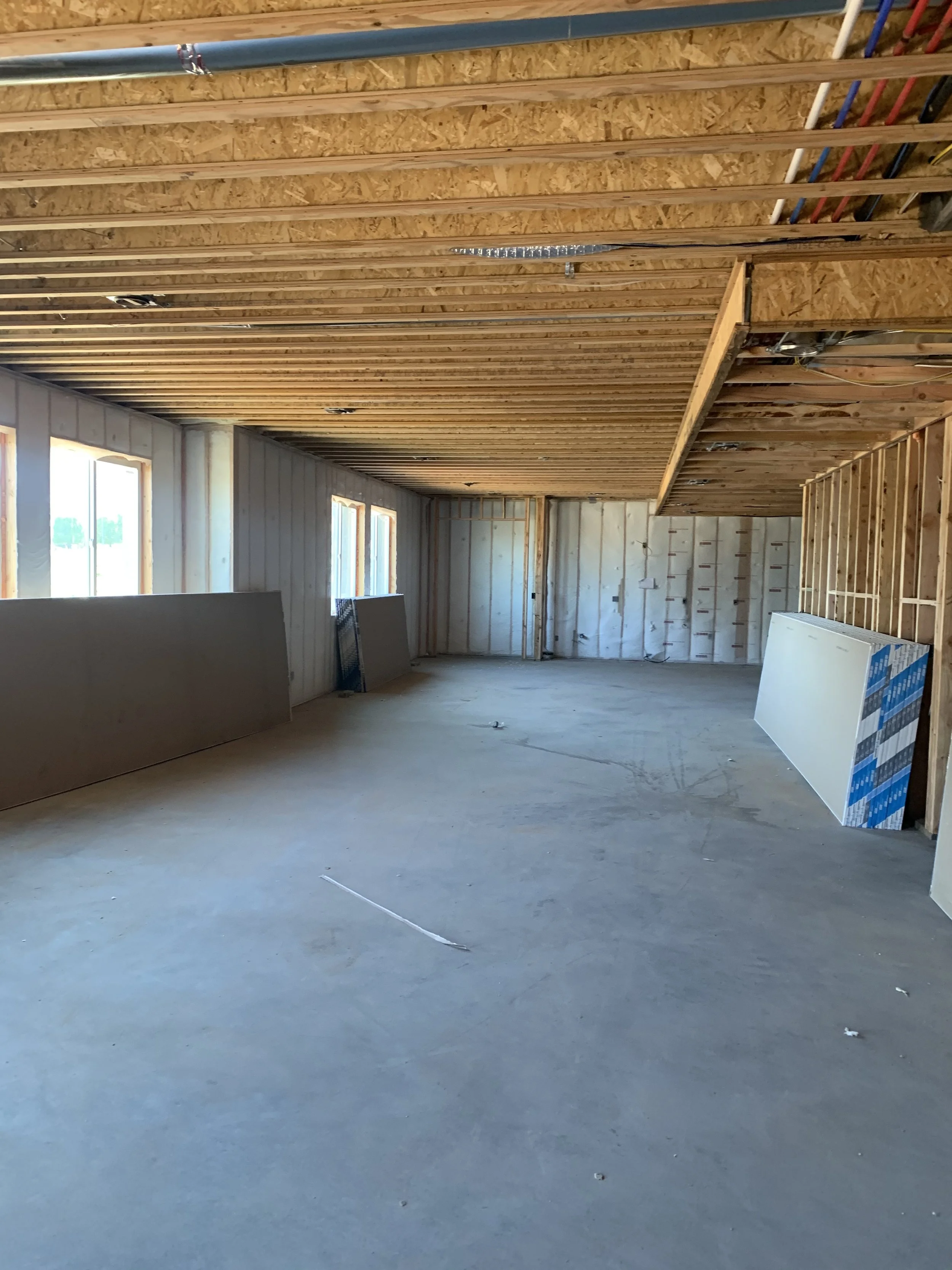 Interior view of a house under construction with exposed wooden framing, unfinished walls, and construction materials on the floor.