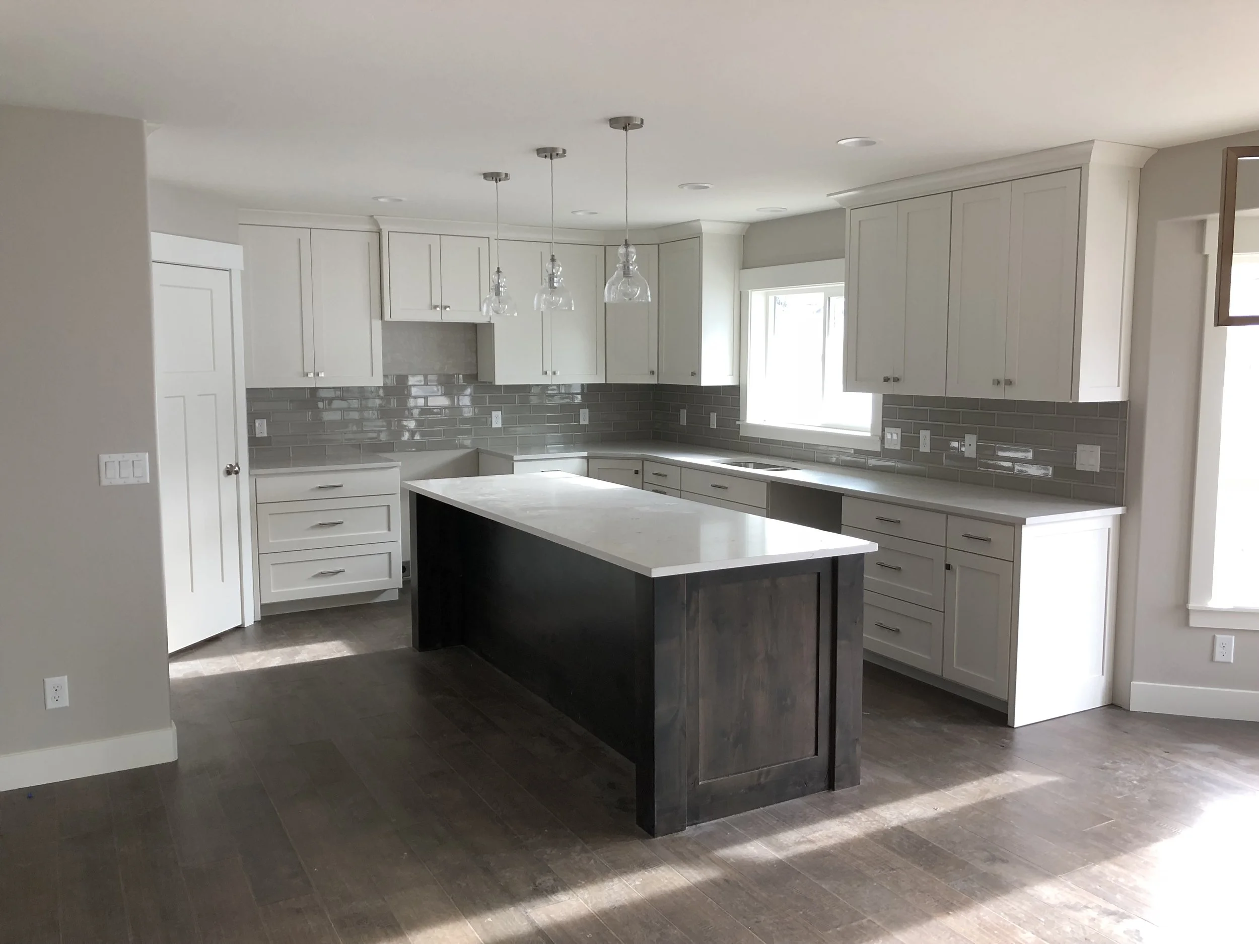 Modern kitchen with white cabinets, gray tile backsplash, dark wood island, and hardwood floors.
