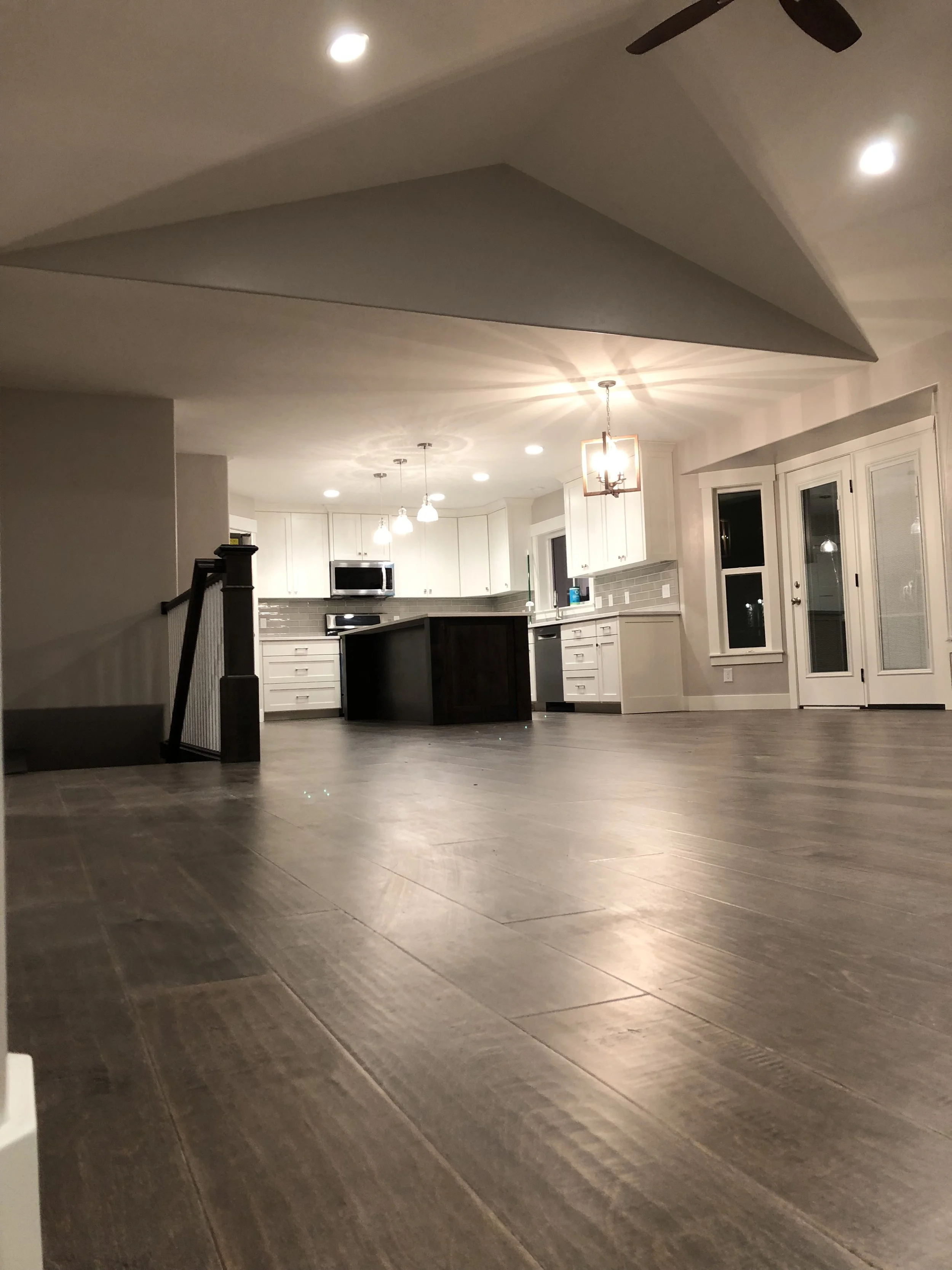 Empty modern kitchen and living space with dark wood flooring, white cabinetry, a center island, and ceiling lights.