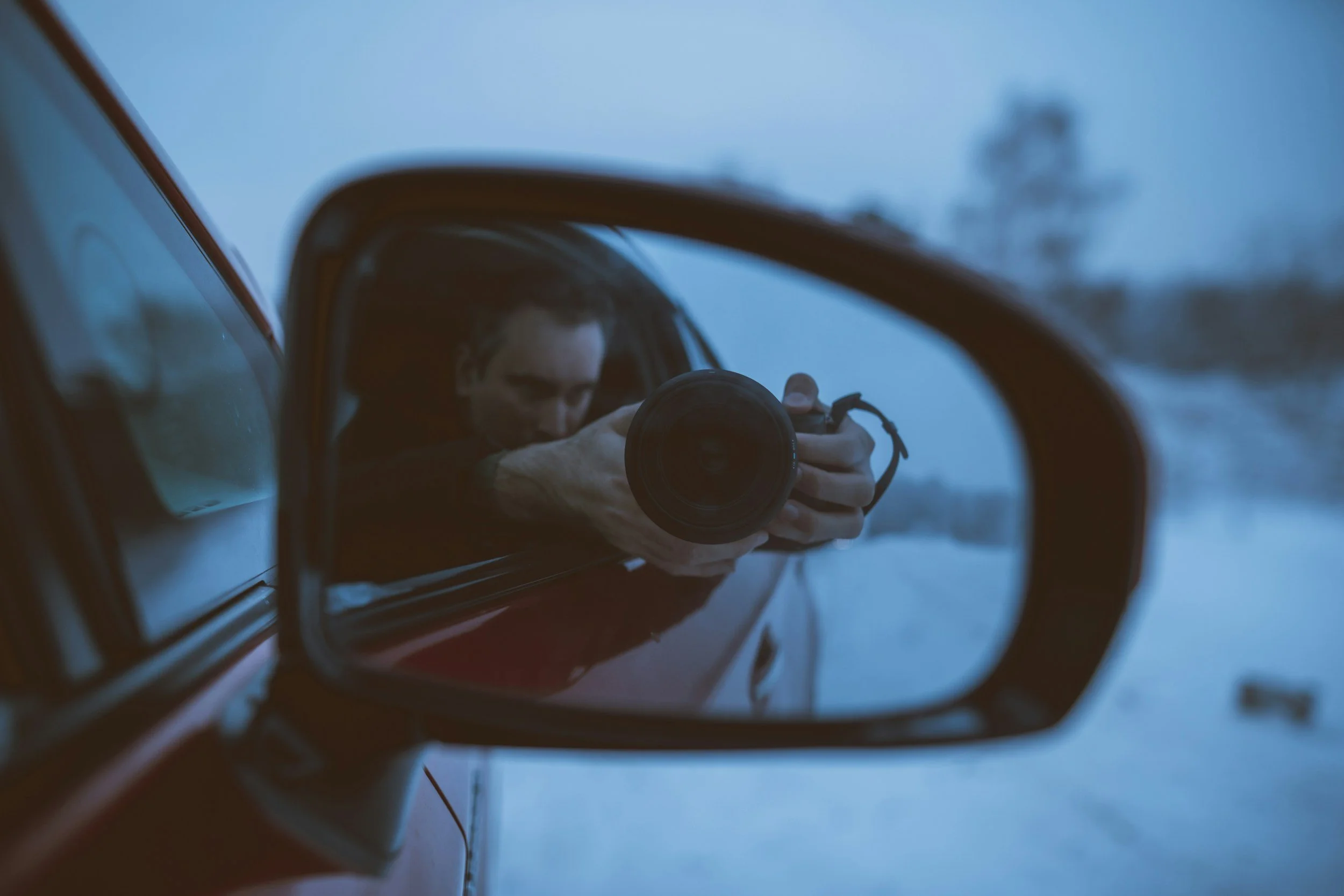 Person taking a photo with a camera in the side mirror of a vehicle during winter.