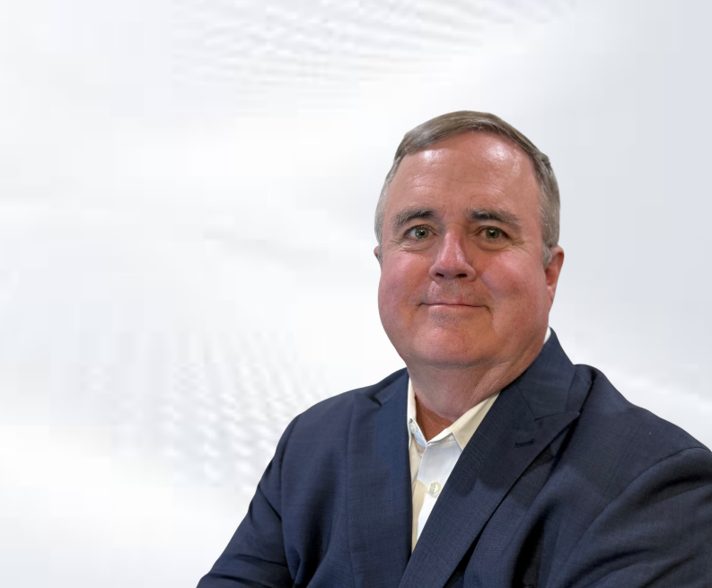A middle-aged man with short gray hair and a slight smile, wearing a navy blue blazer and white shirt, posing in front of a plain white background.