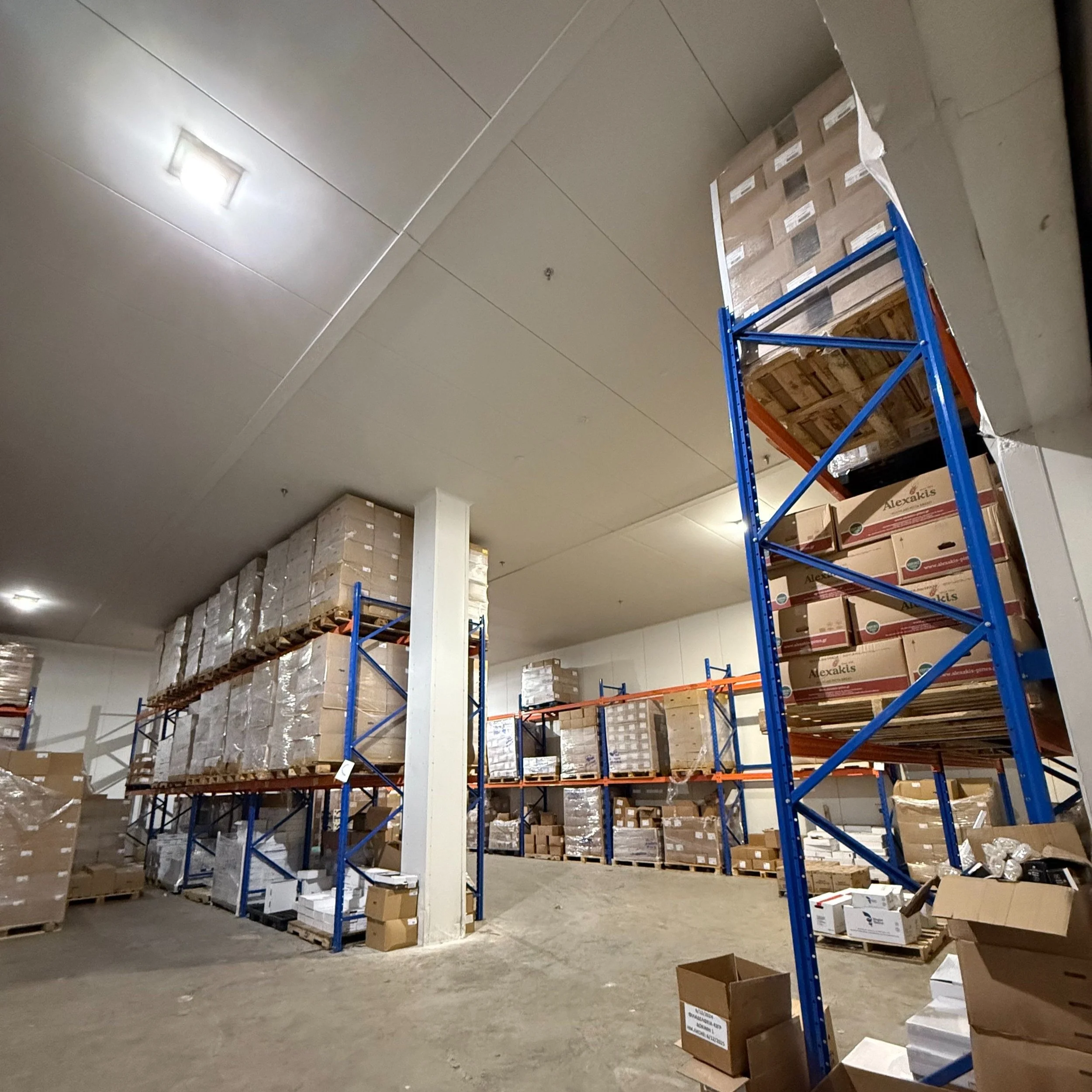 Warehouse storage area with blue metal shelving holding boxes, some stacked high, and some boxes on the floor.