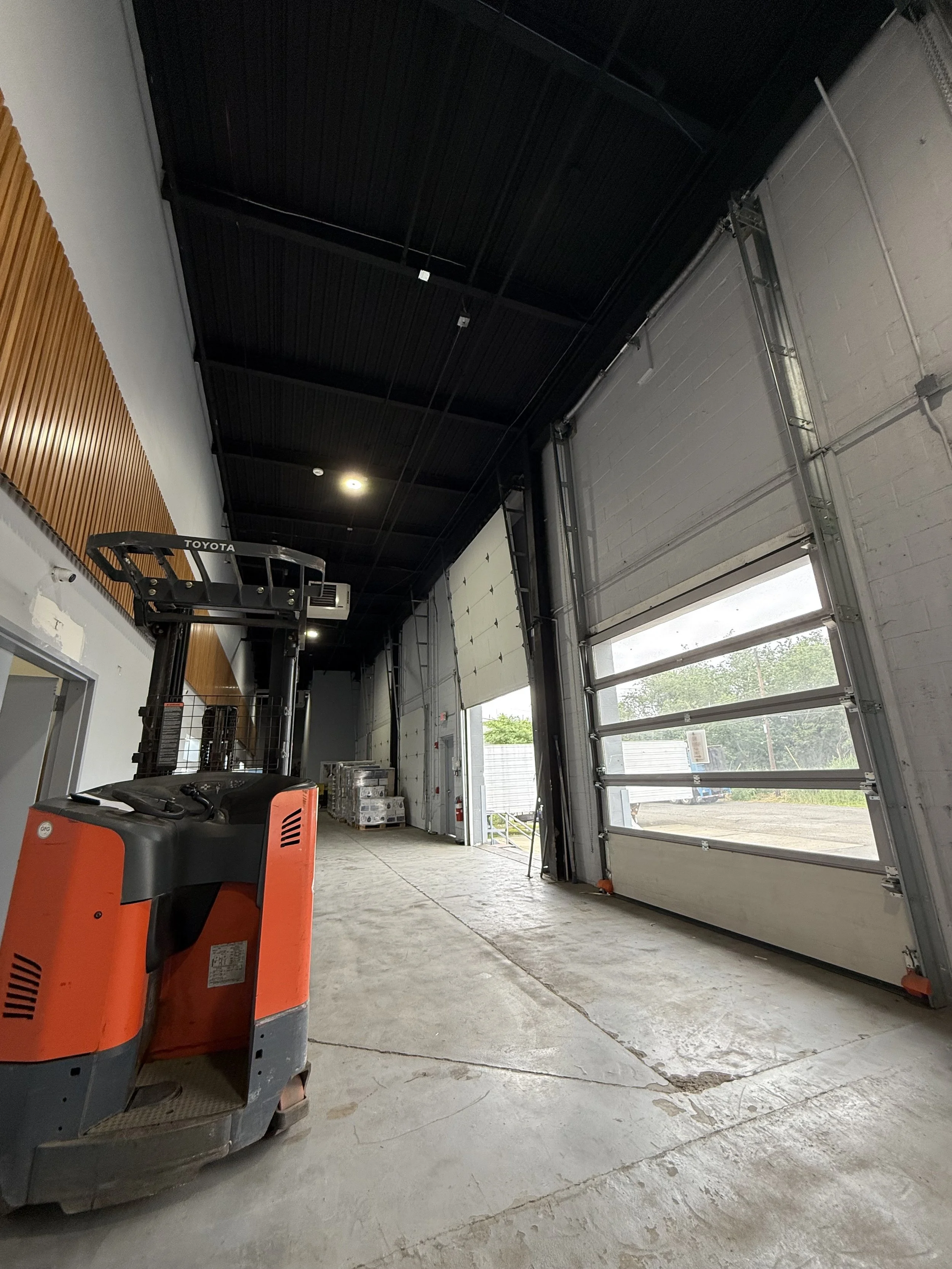 Empty industrial warehouse with large roll-up garage doors, a forklift, and concrete floor.