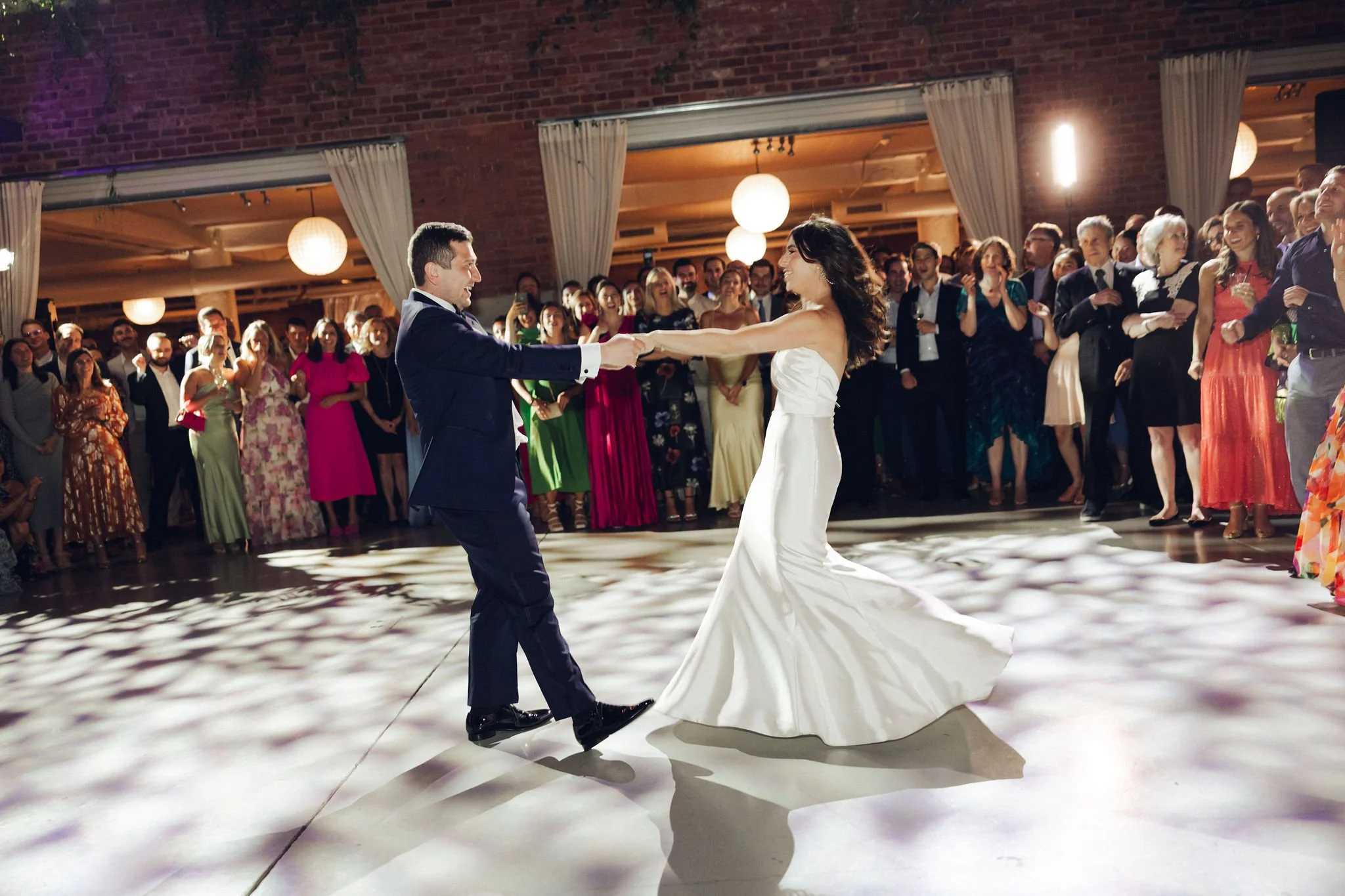 Bride and groom dancing at wedding reception with guests in background.