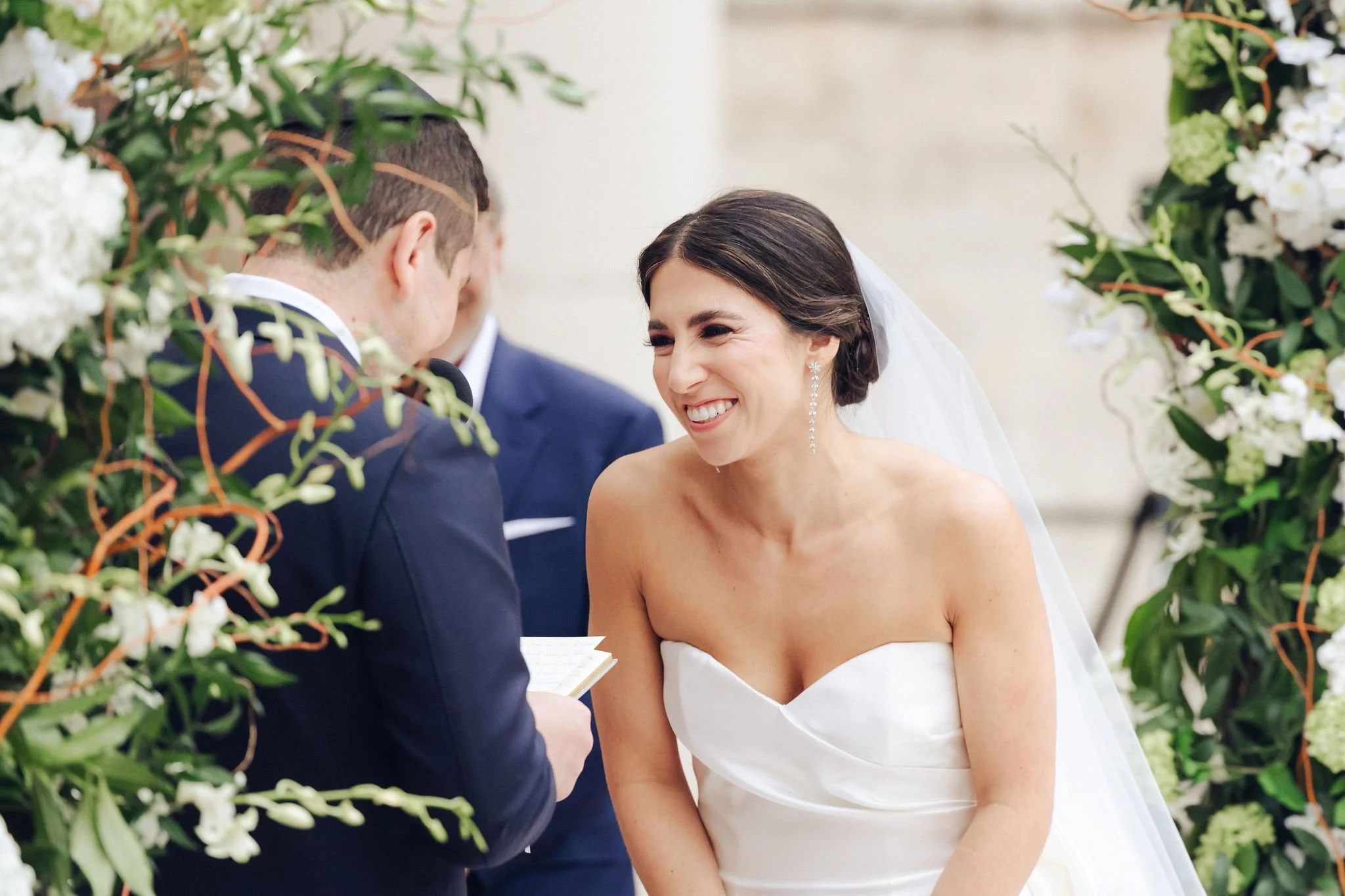 Bride and groom exchanging vows at an outdoor wedding ceremony, surrounded by white floral decorations.
