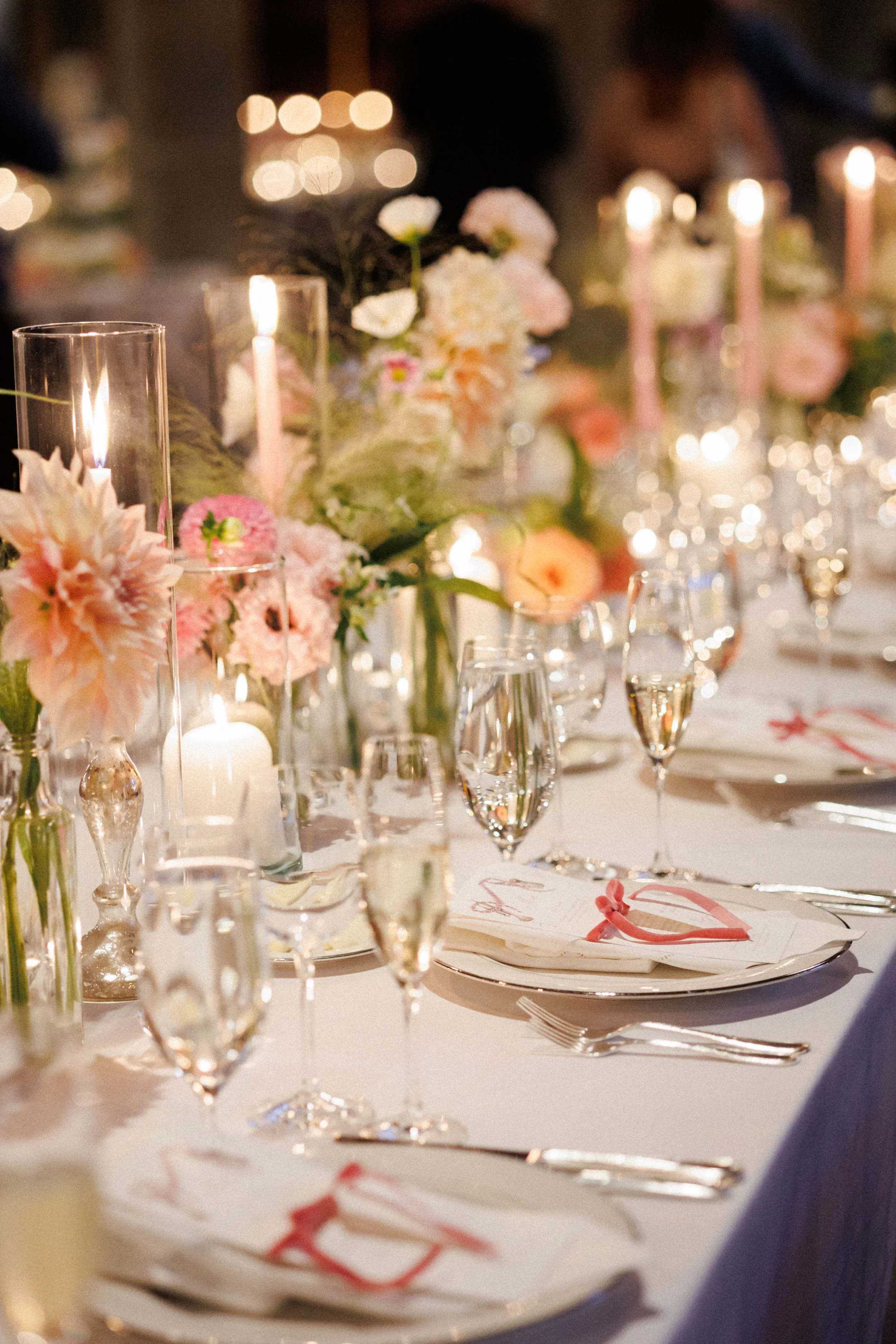 Elegant table setting with pink and white floral arrangements, candles, and champagne glasses for a celebration or wedding.