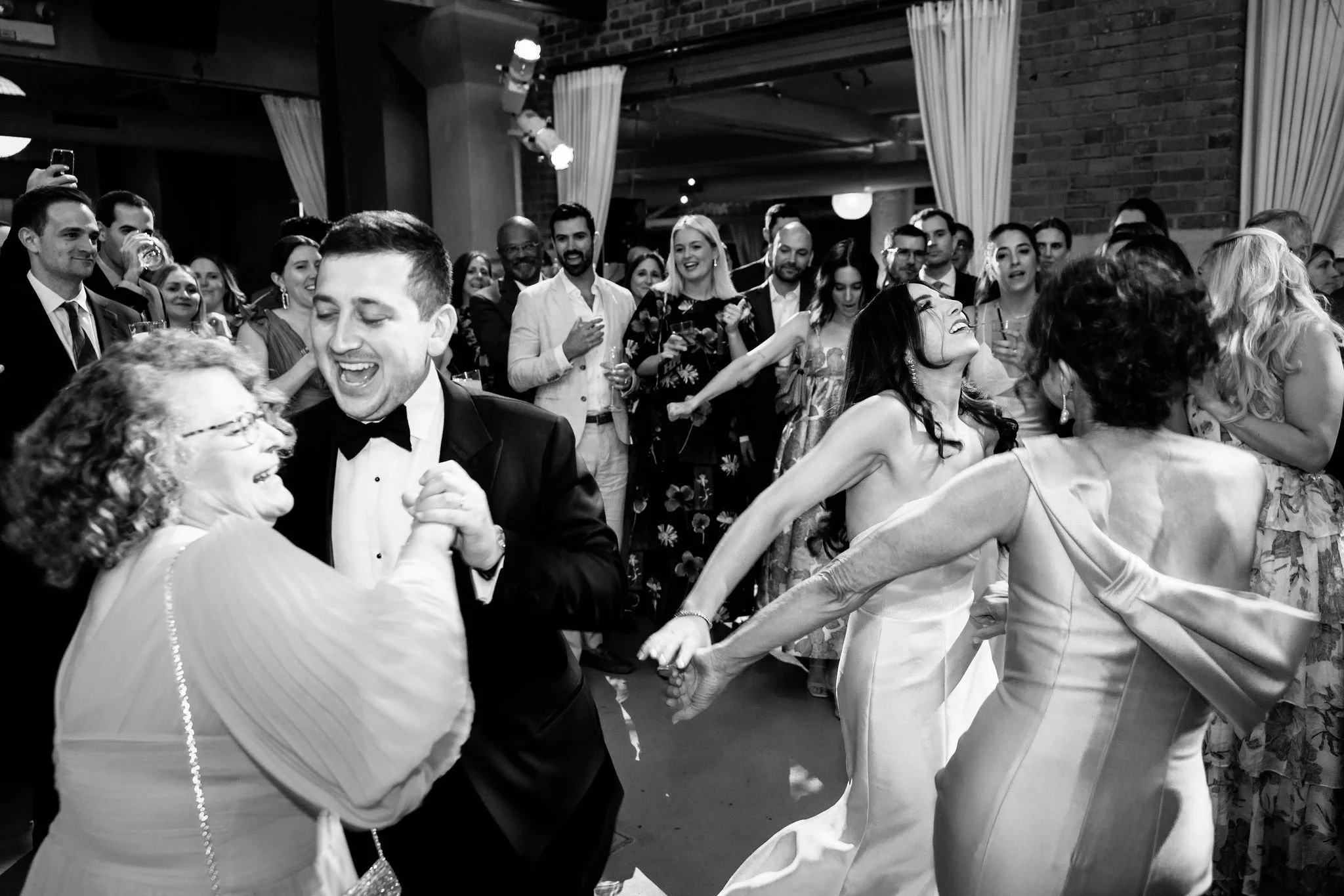 People dancing and celebrating at a lively party or wedding reception, with a group laughing and enjoying themselves.