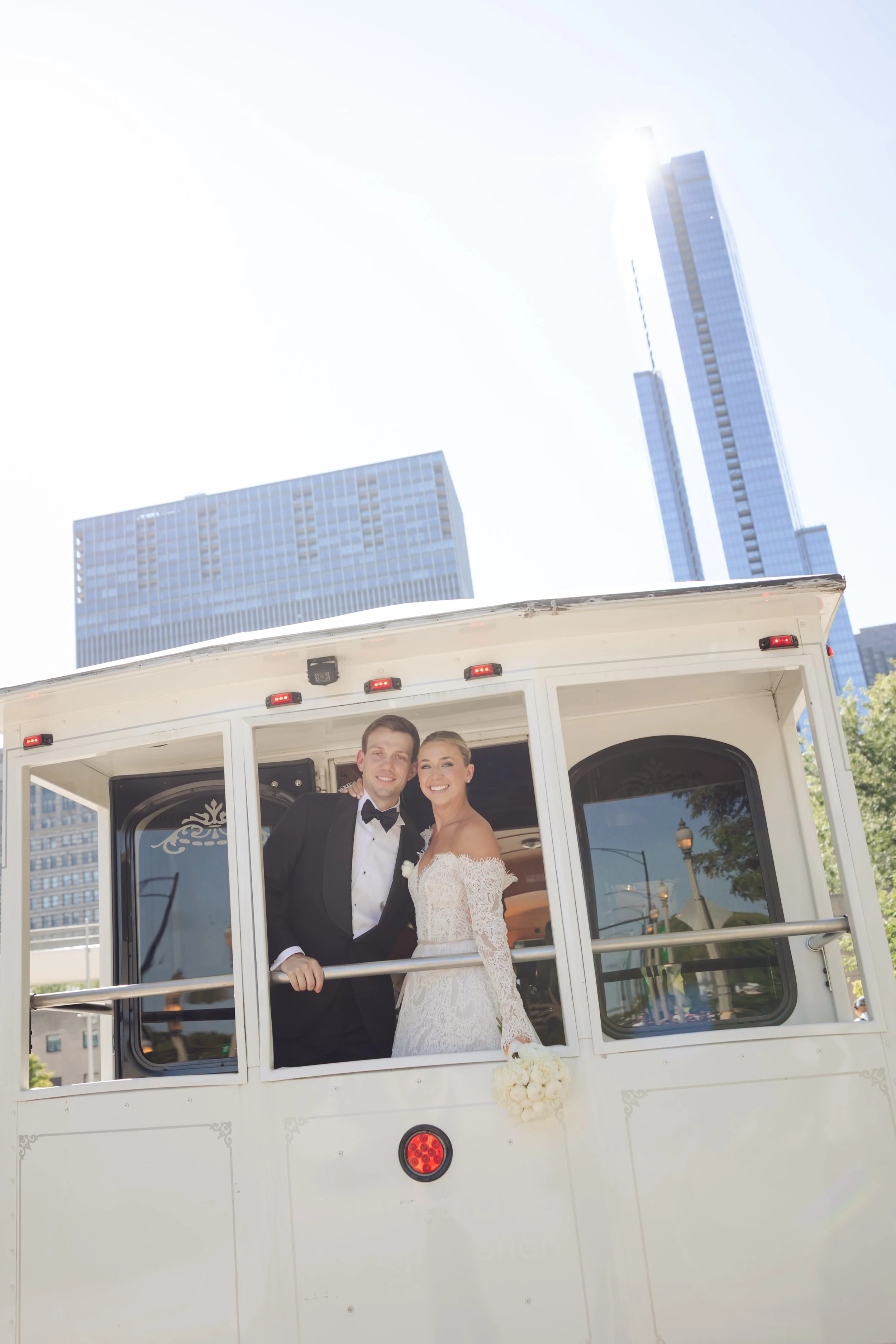 Bride and groom smiling in a white trolley with city skyscrapers in the background