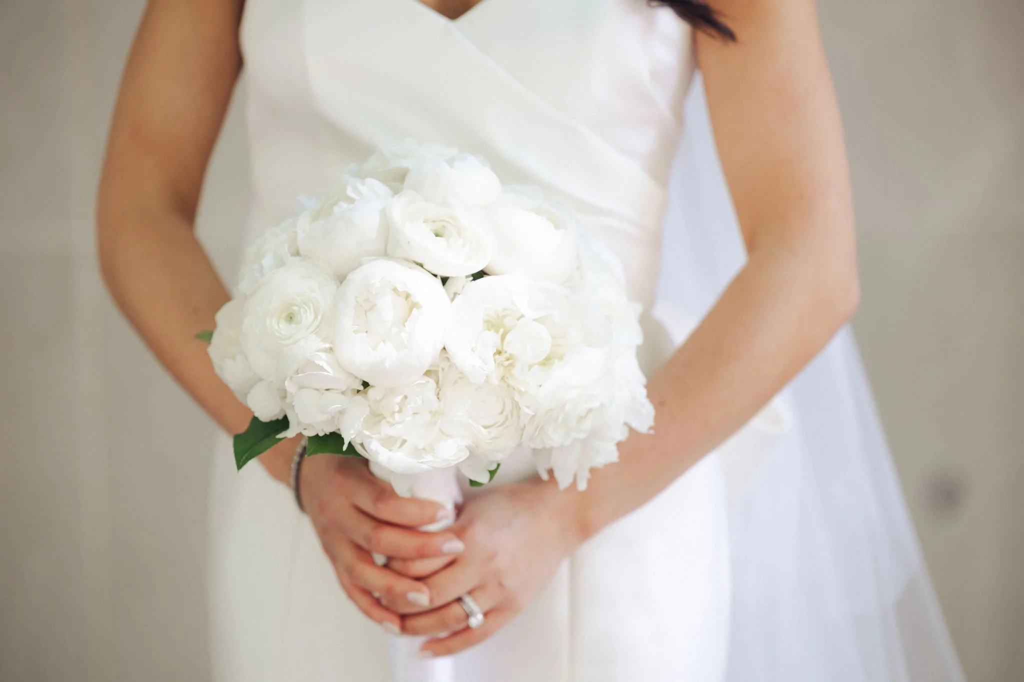 A bride in a white wedding dress holding a bouquet of white flowers, including roses and peonies.