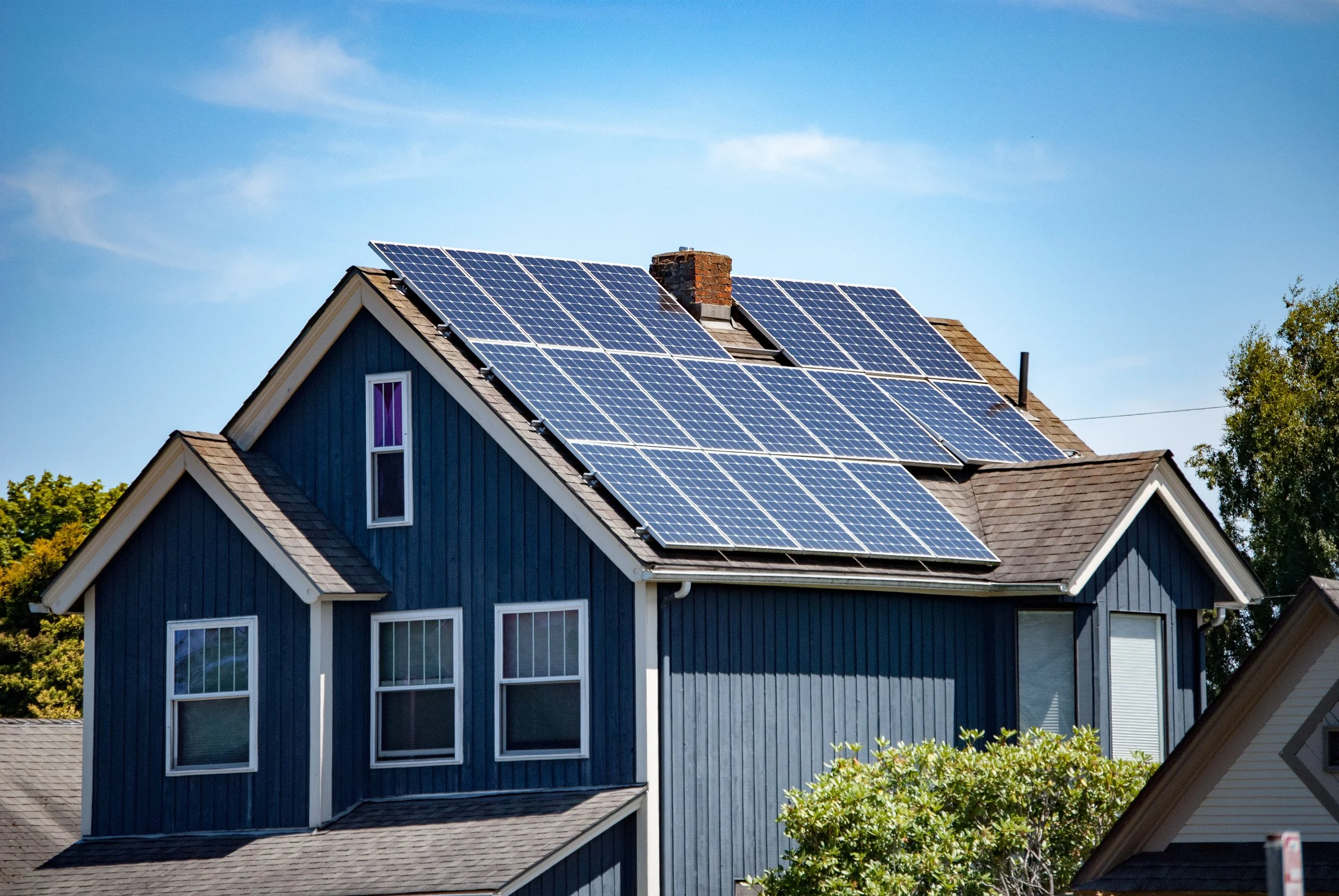 A blue house with multiple solar panels installed on its roof, under a clear blue sky.