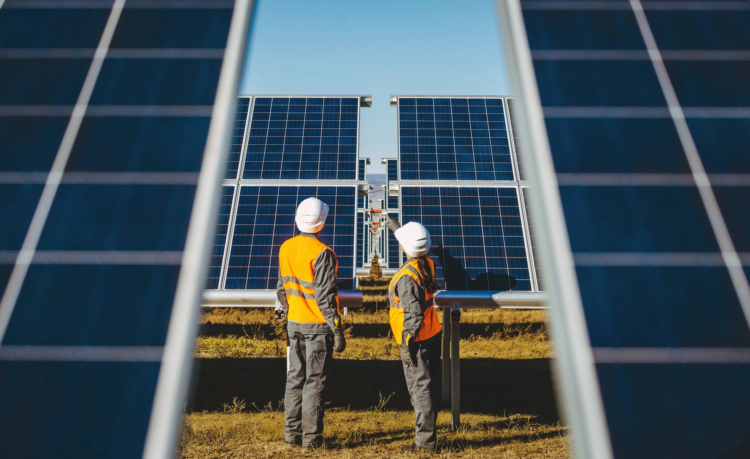 Two workers in safety vests and helmets inspecting solar panels at a solar farm.