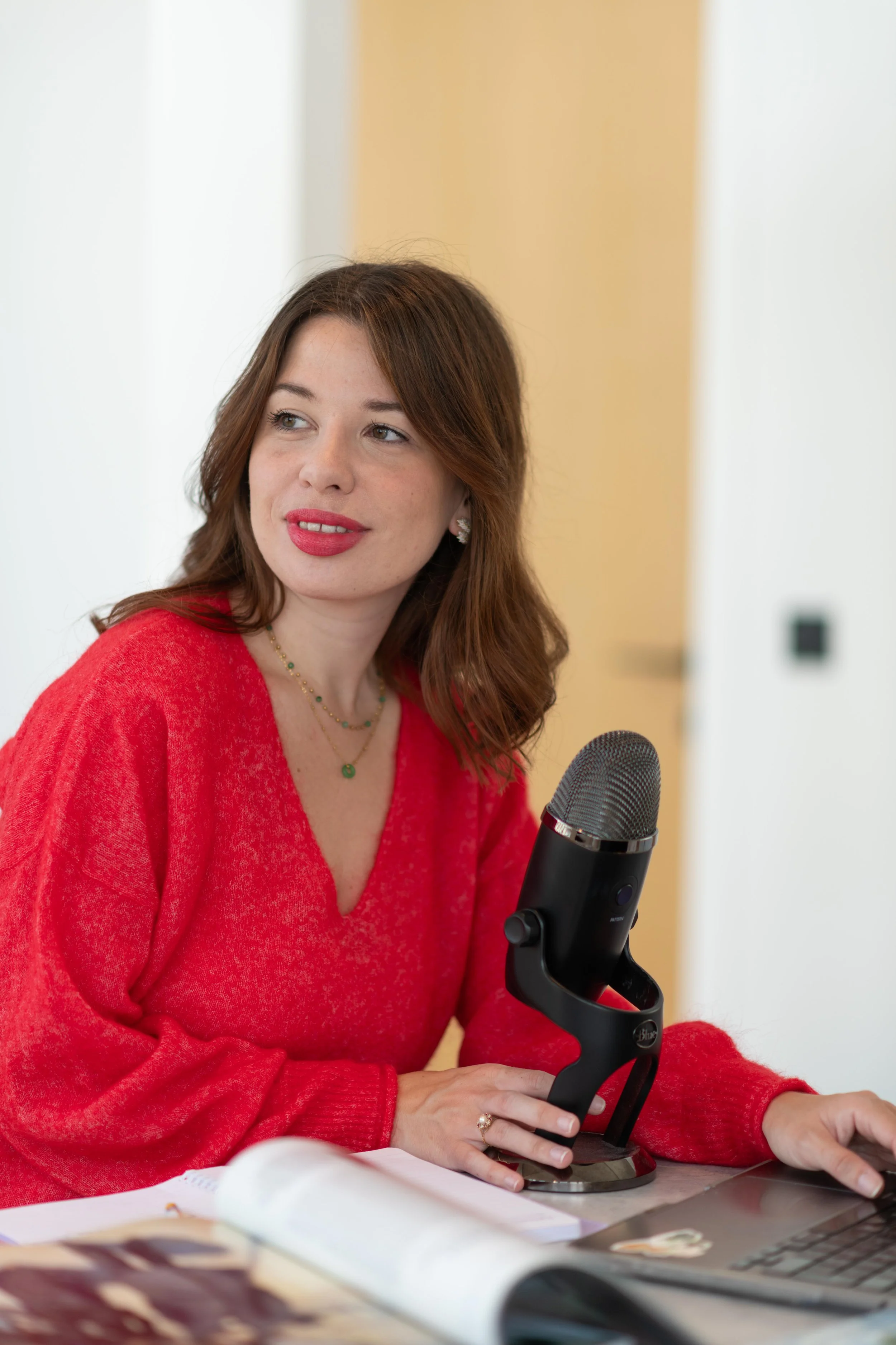 Femme brune, Eva LECONTE, du podcast Comme un gant,  avec chemisier rouge près d'un microphone en studio ou bureau.