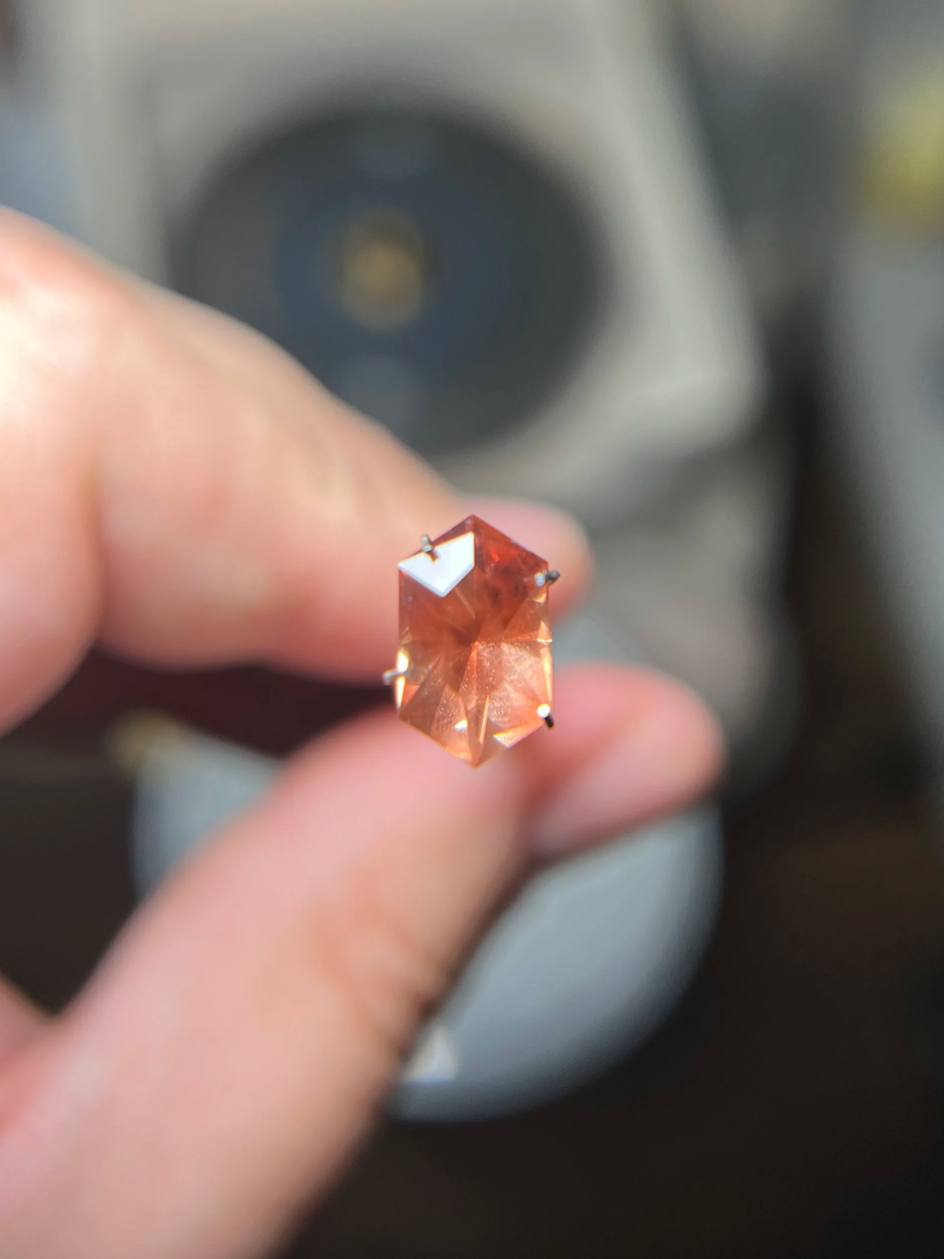 Close-up of a peach-colored Oregon sunstone held between fingers with a blurred background.