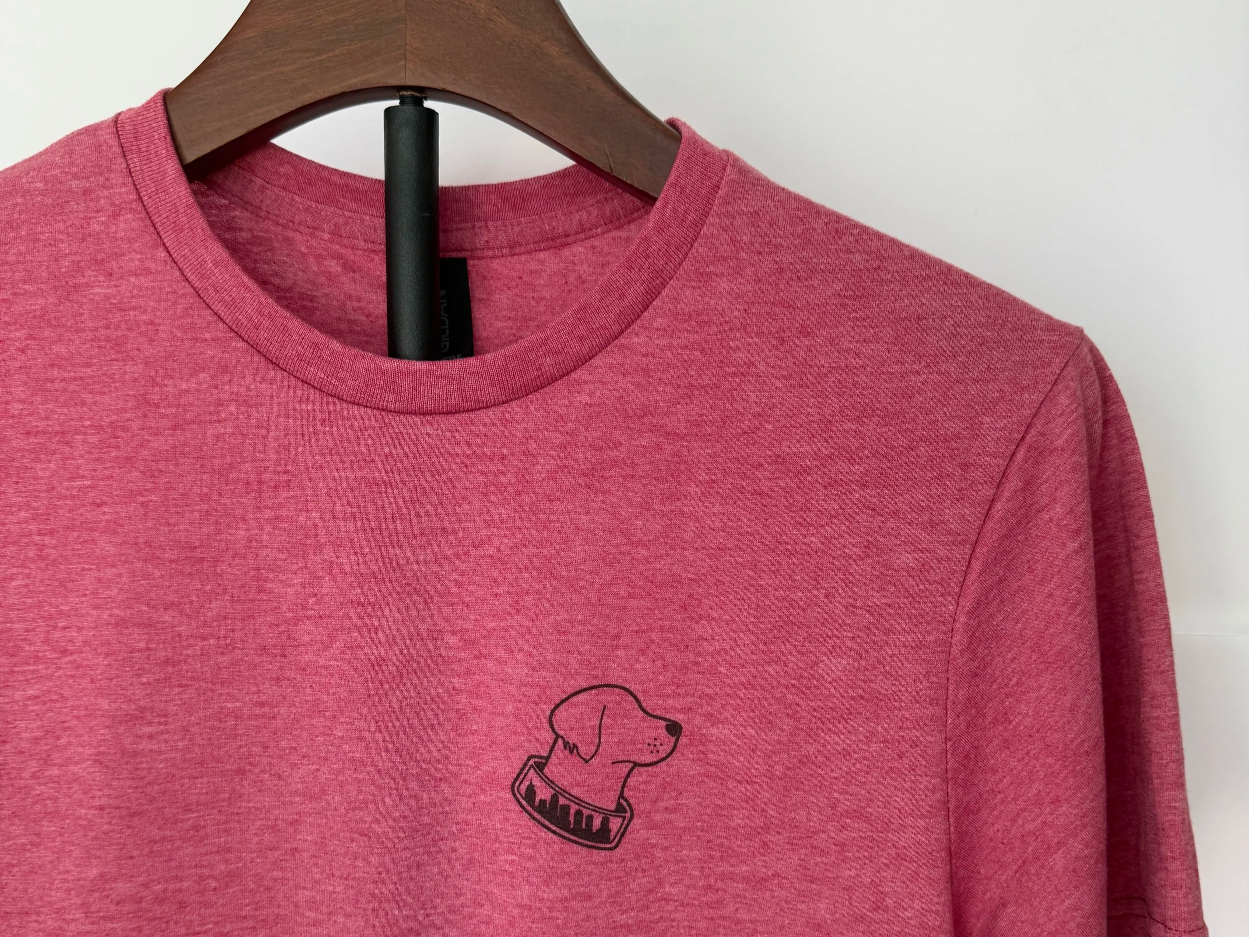 Pink sweatshirt hanging on a wooden hanger with a small black outline of a dog's head and collar printed on the front.