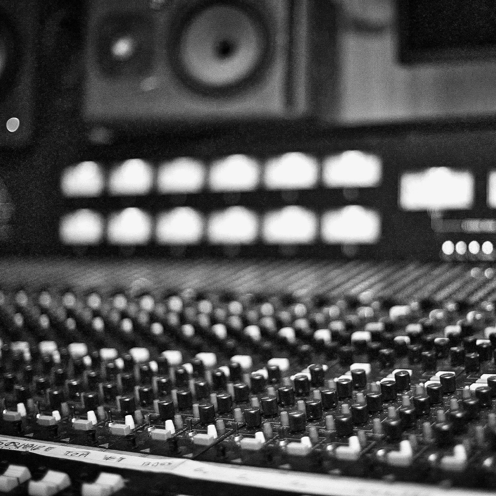 Close-up of an audio mixing console with numerous knobs and controls, black and white photo.