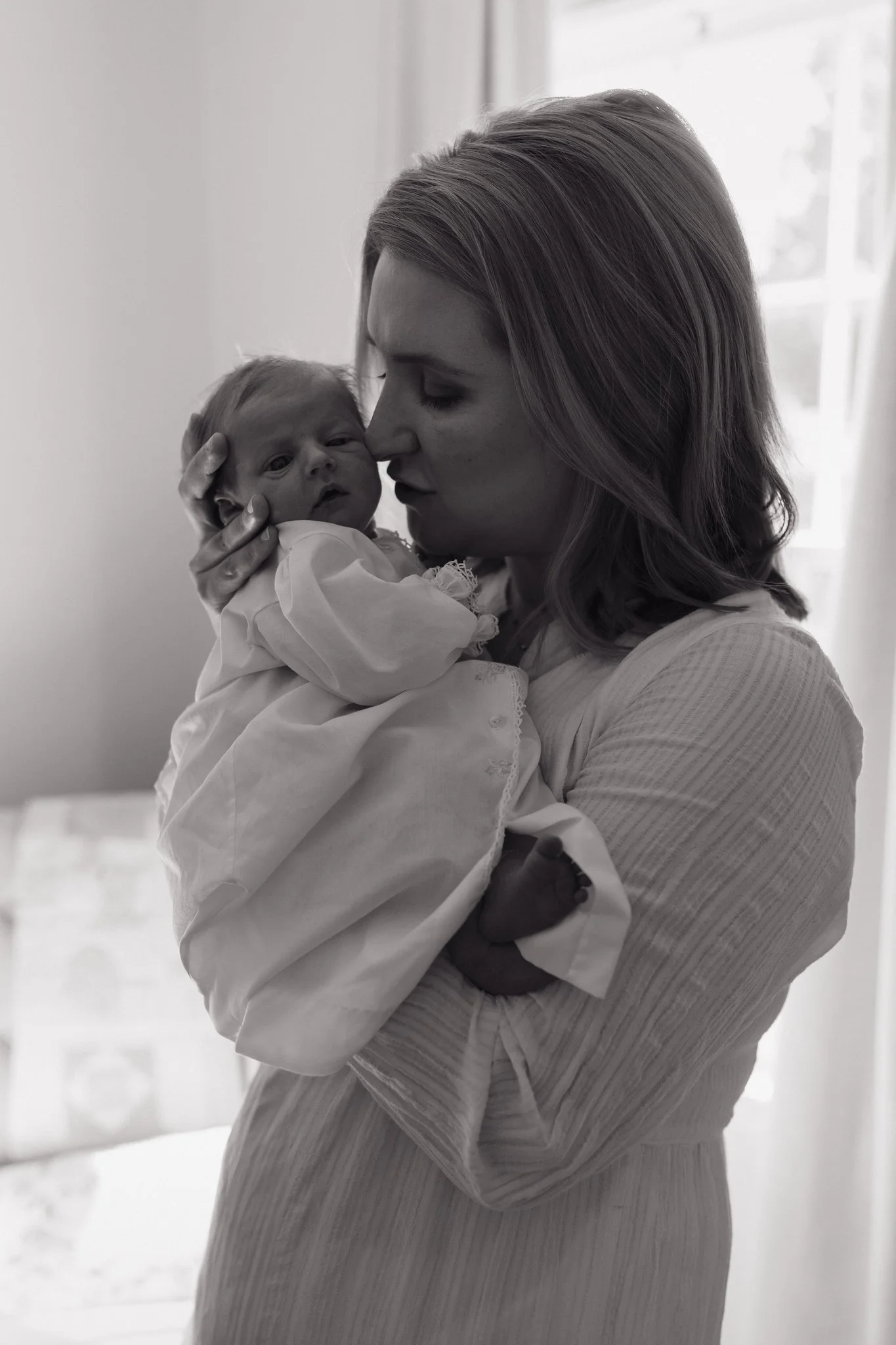 A woman holding a newborn baby indoors near a window, both facing each other closely, with the woman gently touching the baby's head. The photograph is in black and white in Memphis, TN. 