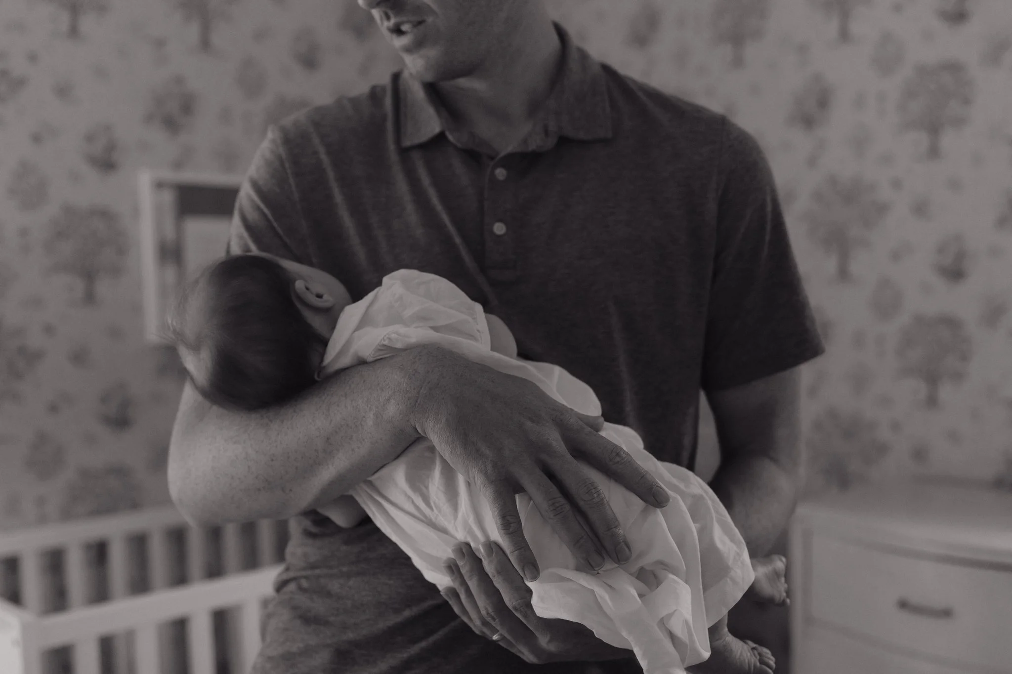 A man wearing a dark shirt holds a newborn baby wrapped in a blanket, smiling and looking down at the infant in Memphis, TN. 
