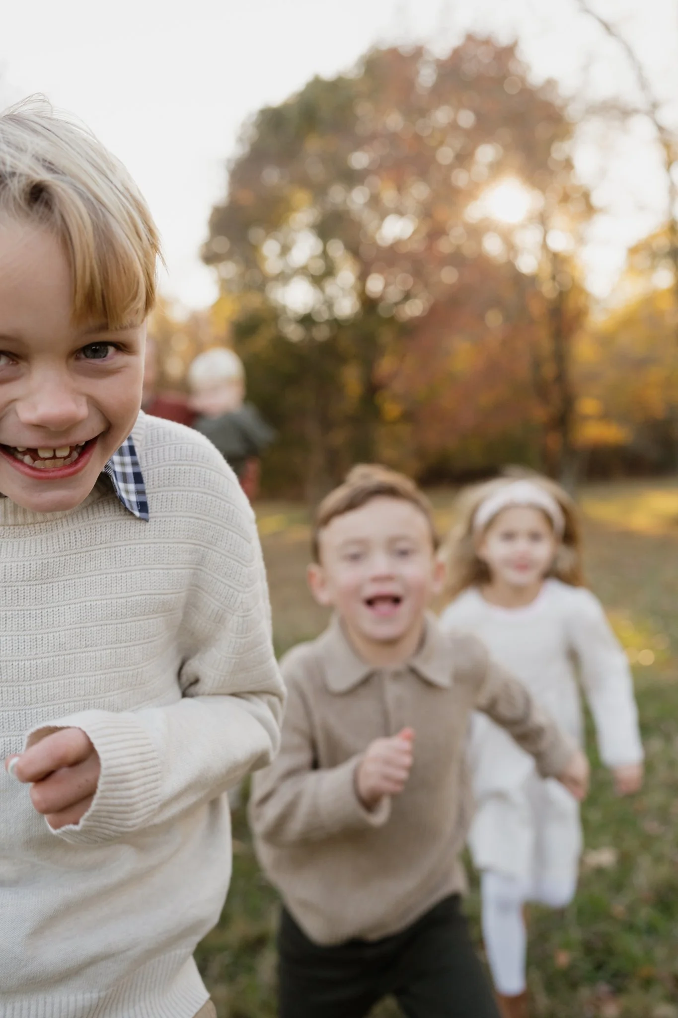 A group of children running outdoors in a park with fall foliage, the sun shining through trees in the background in Memphis, TN. 
