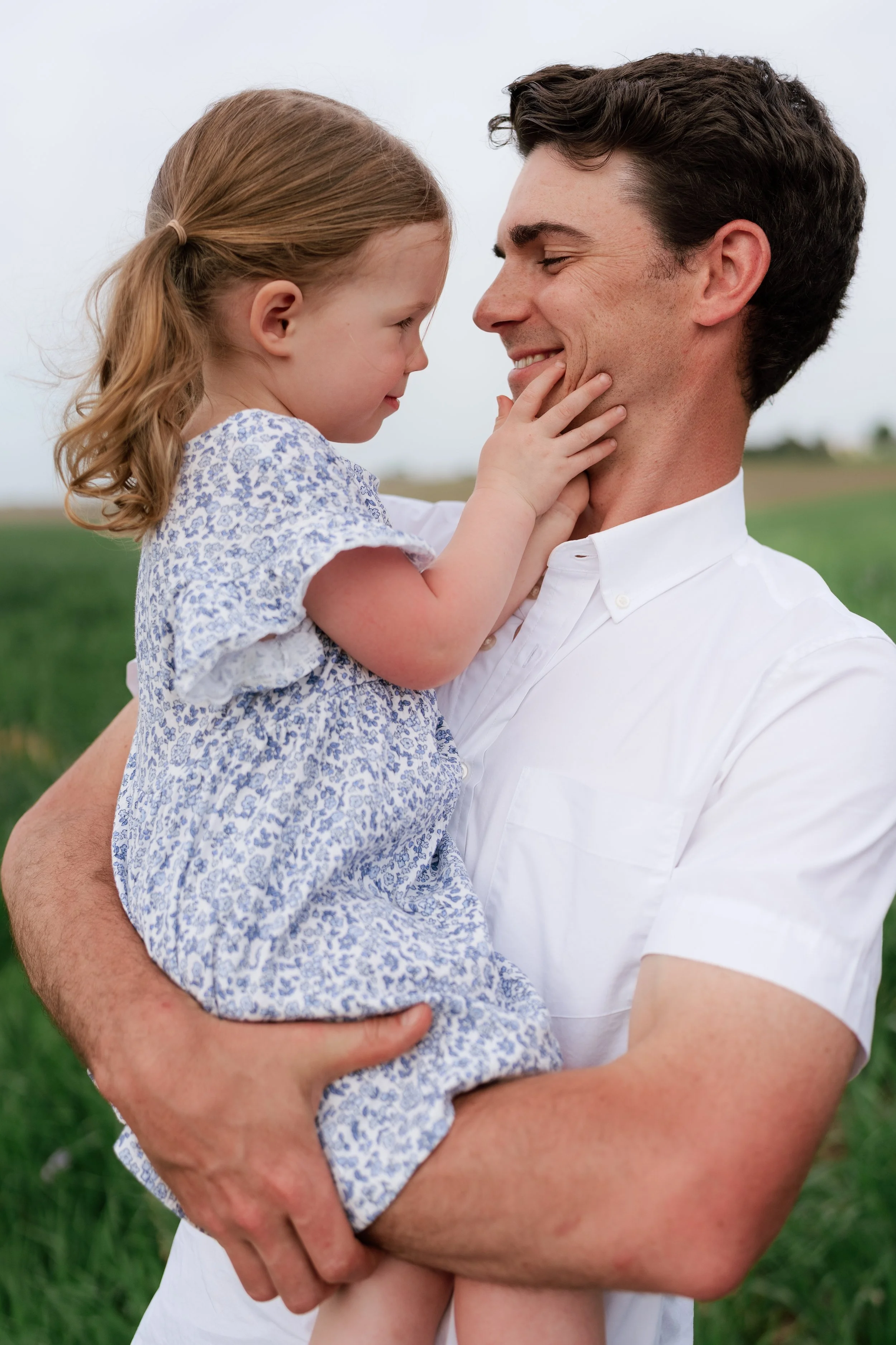 A man holding a young girl in his arms outdoors in a field with green grass, smiling and touching foreheads on a farm outside of Memphis, TN. 