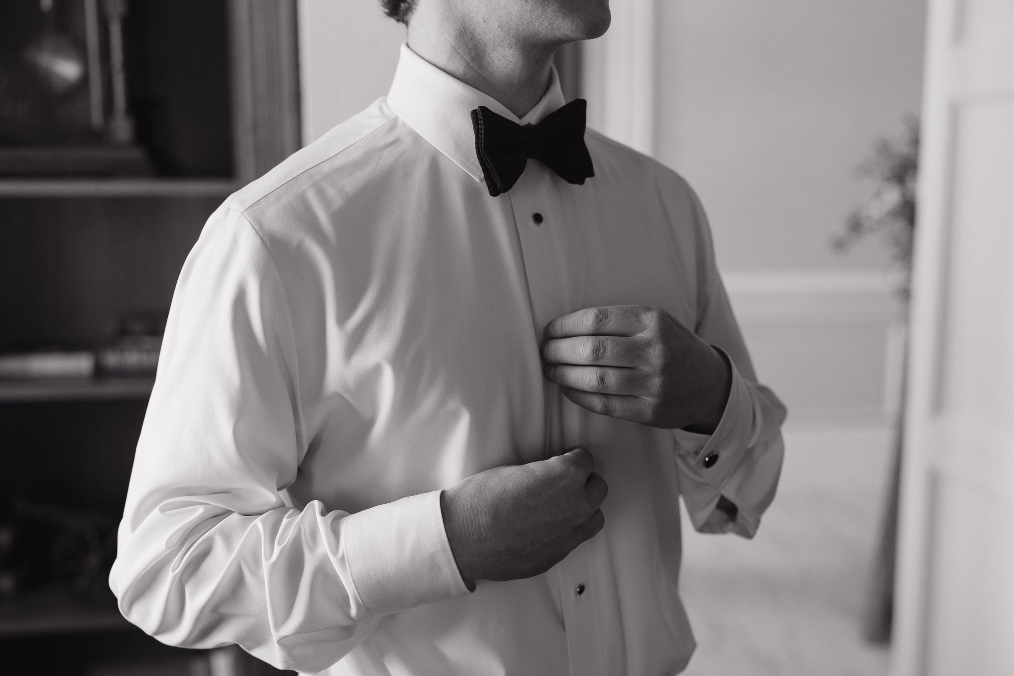 A man dressed in a white shirt with black buttons and a black bow tie, adjusting his shirt cuff with one hand while the other is near the chest, in a black and white photograph in Memphis, TN. 