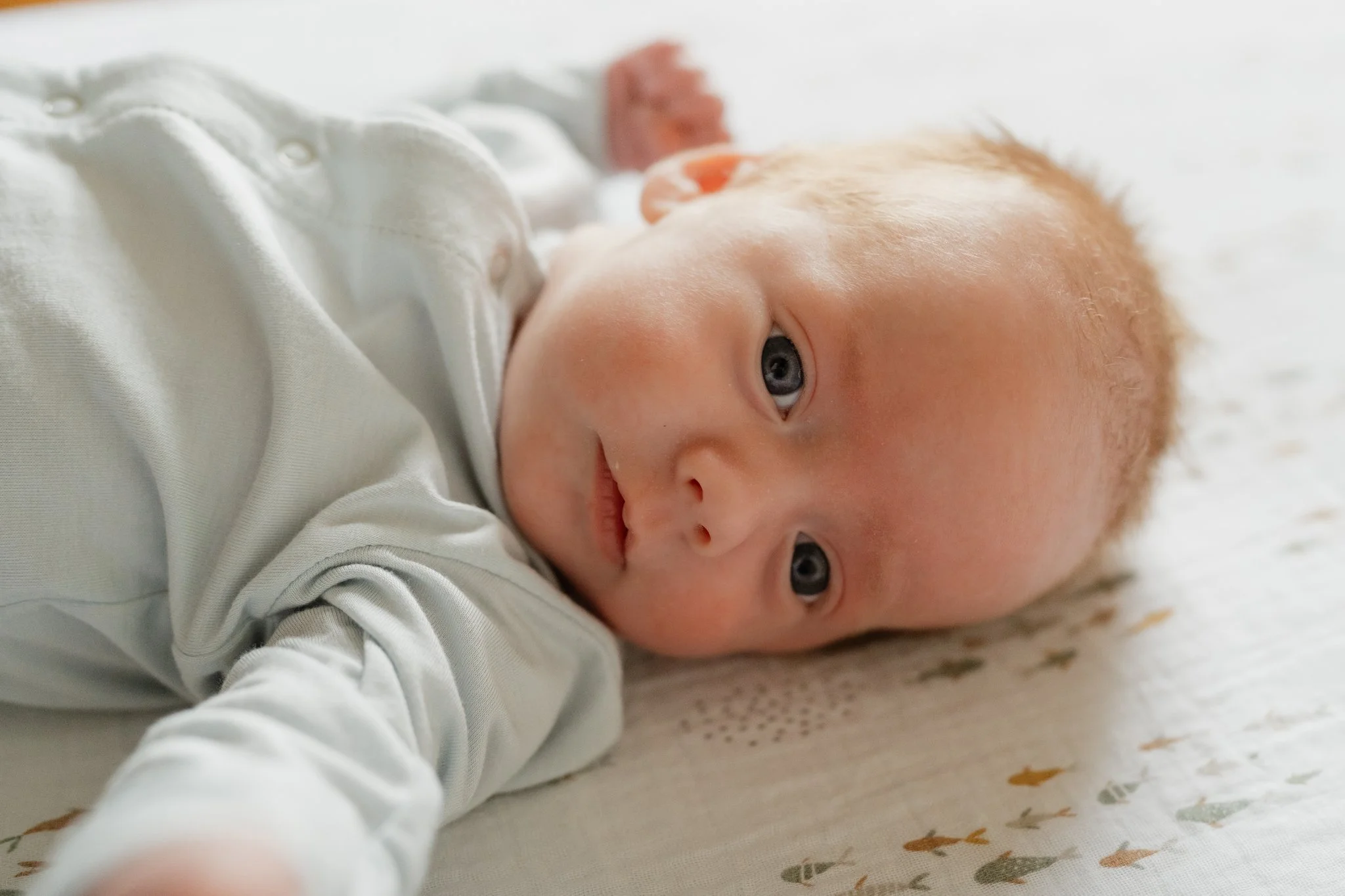 Close-up of a baby with red hair lying down on a white blanket with colorful patterns, looking at the camera in Memphis, TN. 