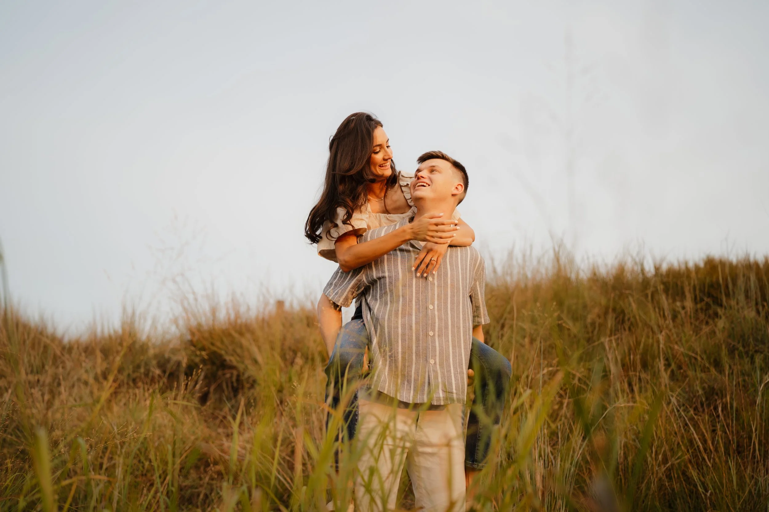 A man giving a piggyback ride to a smiling woman in a field of tall grass during sunset in downtown Memphis, TN. 