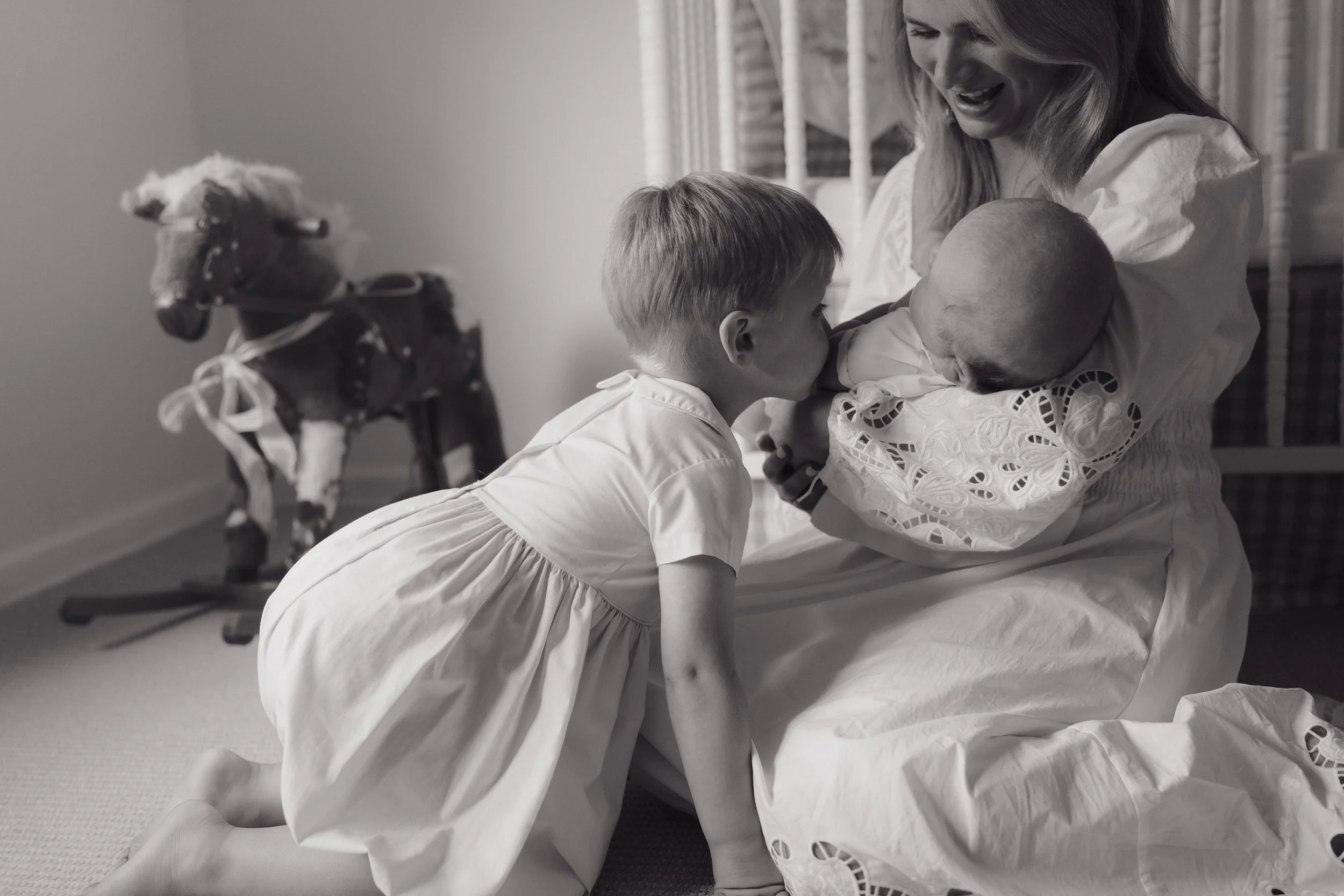 A woman holding a newborn baby and a young girl, all dressed in white, with a horse in the background. The woman is smiling and the children are looking at the baby in Memphis, TN. 