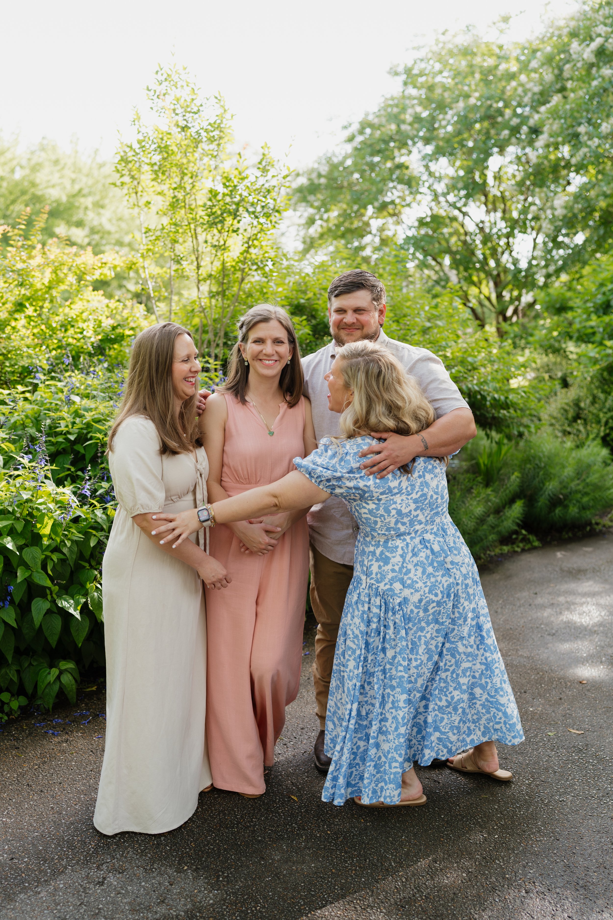 A group of five adults happily hugging and chatting outdoors in a lush, green garden on a sunny day in Memphis, TN. 