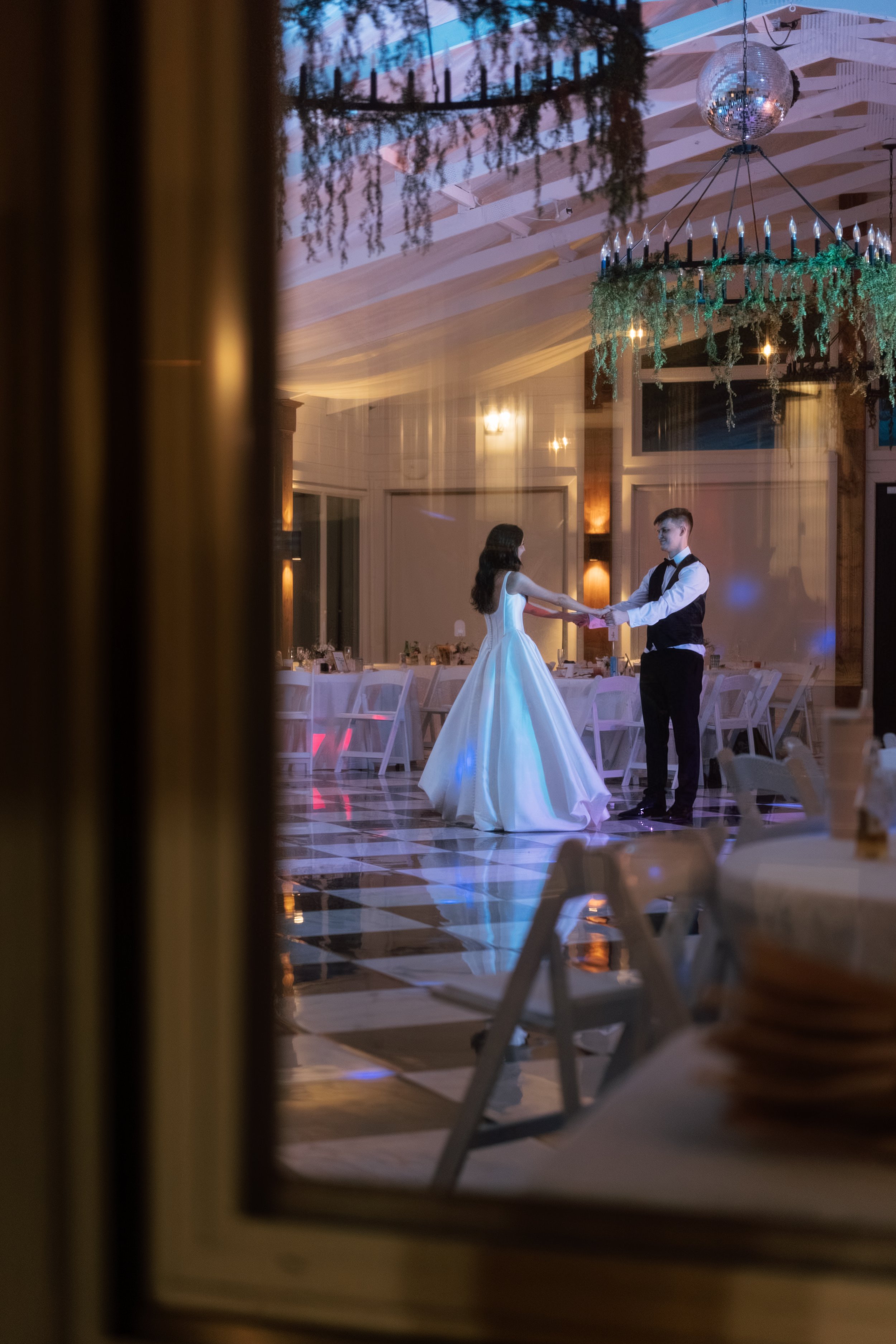A bride and groom are dancing at their wedding reception inside a decorated hall, seen through a window in Memphis, TN. 