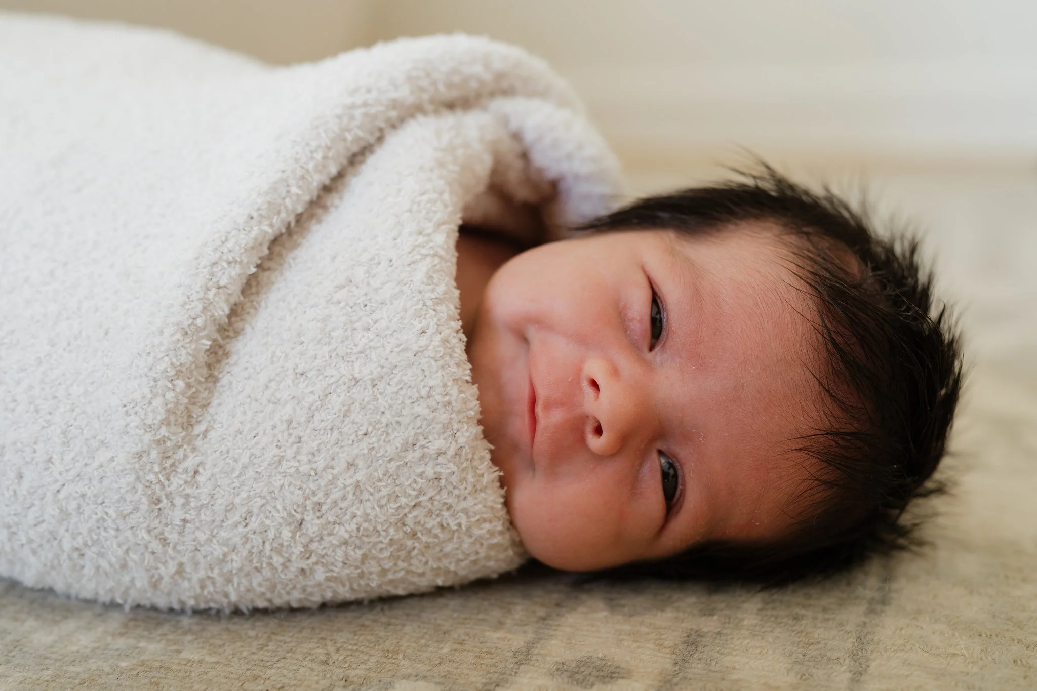 Close-up of a sleeping baby with dark hair wrapped in a soft beige towel.