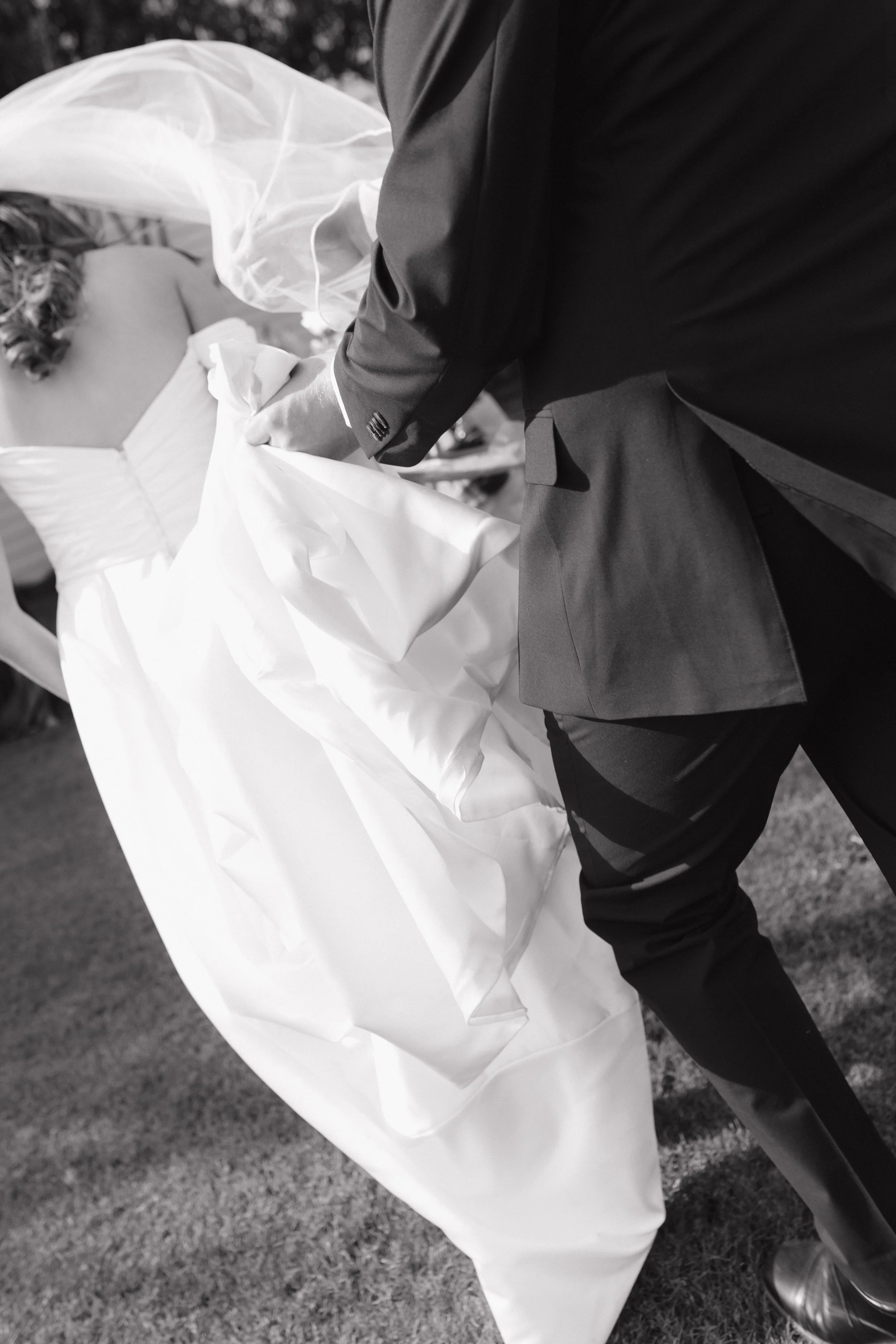 A black and white photo of a man in a suit dancing with a woman in a wedding dress outdoors. The focus is on their lower bodies and the man's hand holding the woman's hand in Memphis, TN. 