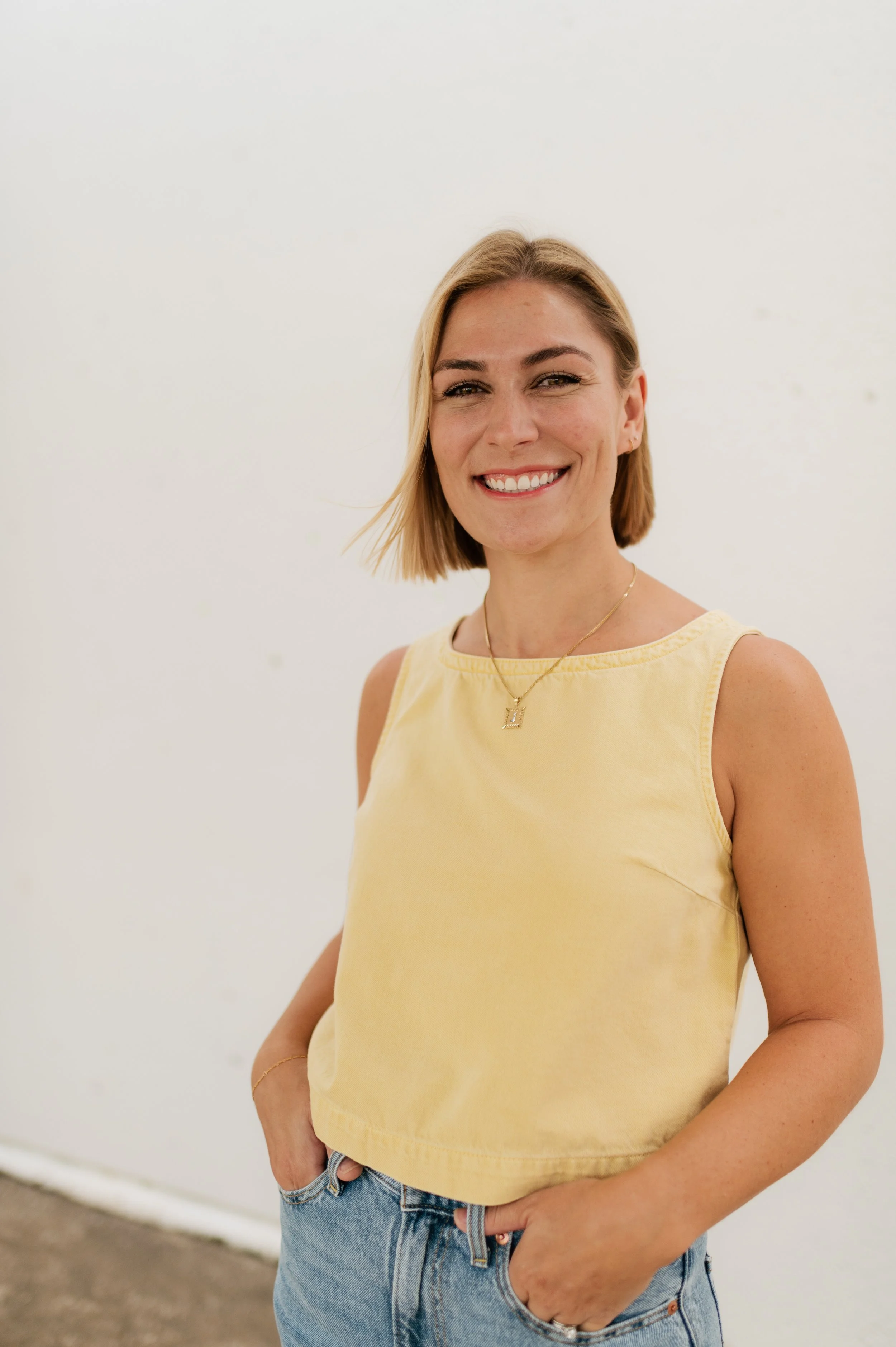 A beautiful wedding photographer in a yellow tank and a camera smiles in Memphis, TN.