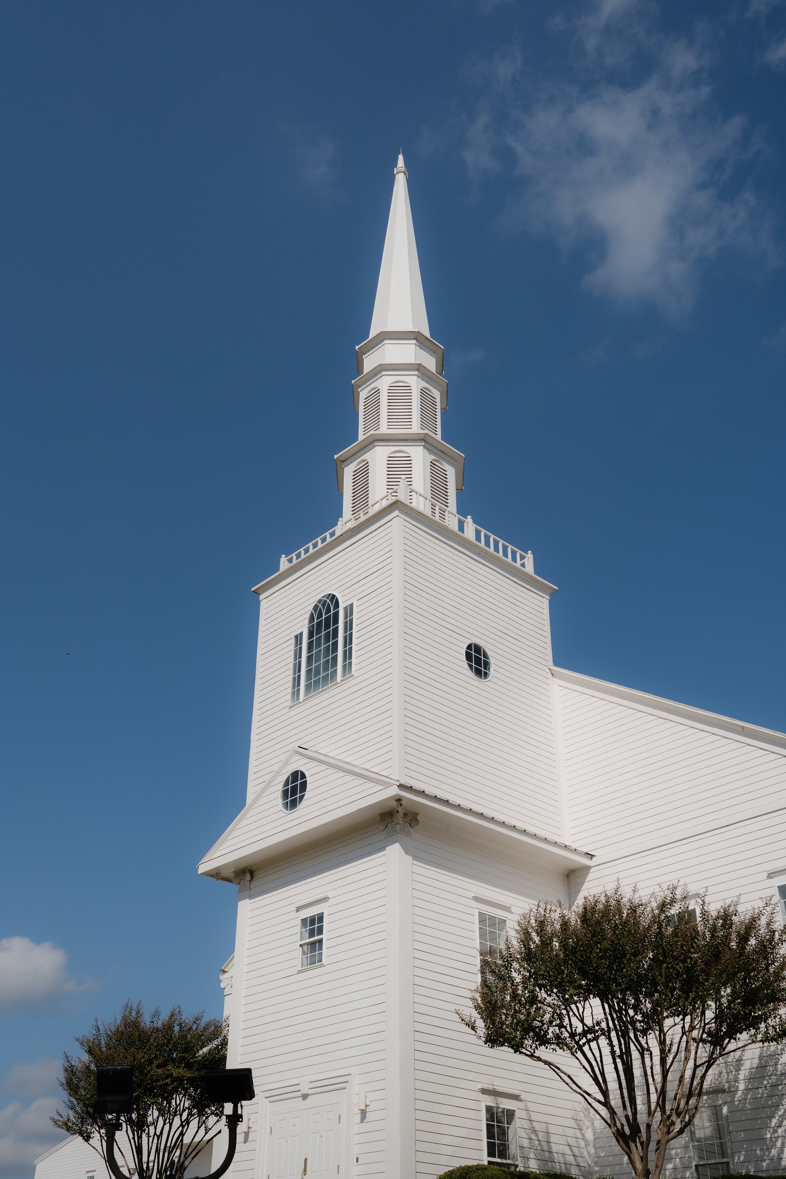 White wedding chapel with a tall steeple against a blue sky with few clouds, surrounded by trees in Memphis, TN. 