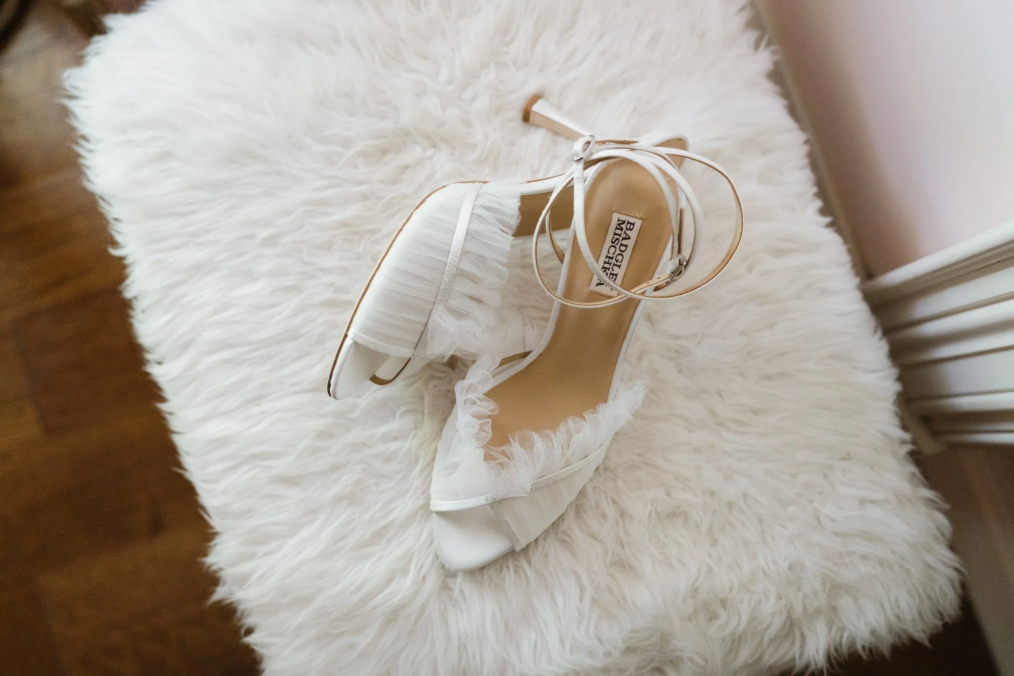 White high-heeled shoe and matching clutch purse with ruffled trim placed on a fluffy white rug in Memphis, TN. 