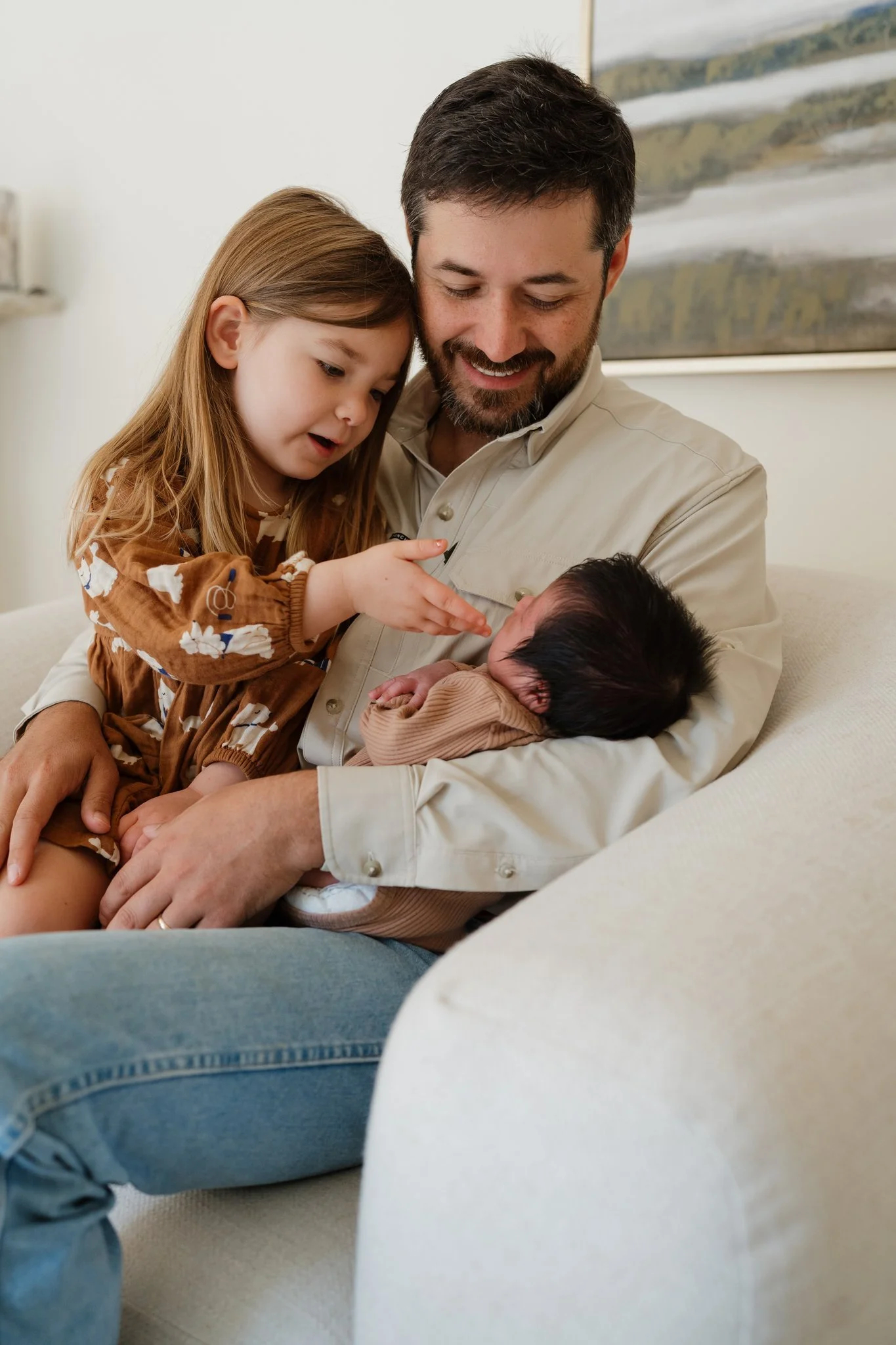 A man holding a newborn baby and a young girl, likely his daughter, looking at the baby with affection in a home setting in Memphis, TN. 