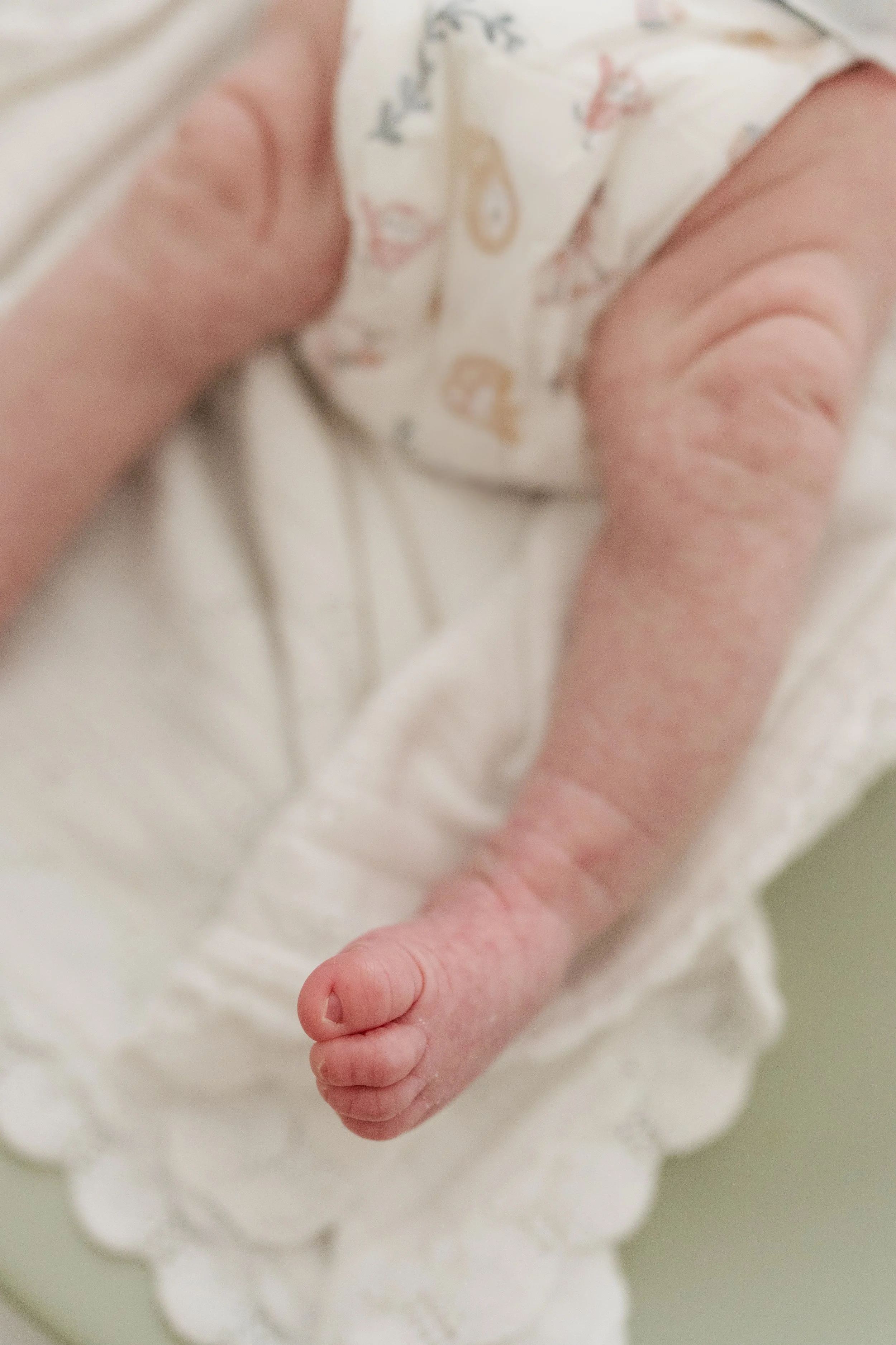 Close-up of an infant's hand and arm, with the baby holding the caregiver's finger, wearing a light-colored shirt with a pattern of small animals in Memphis, TN. 