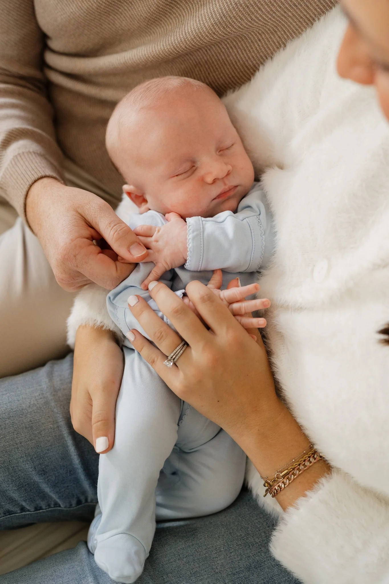 A sleeping baby being held gently, surrounded by adults' hands, with a soft blanket nearby in Memphis, TN. 