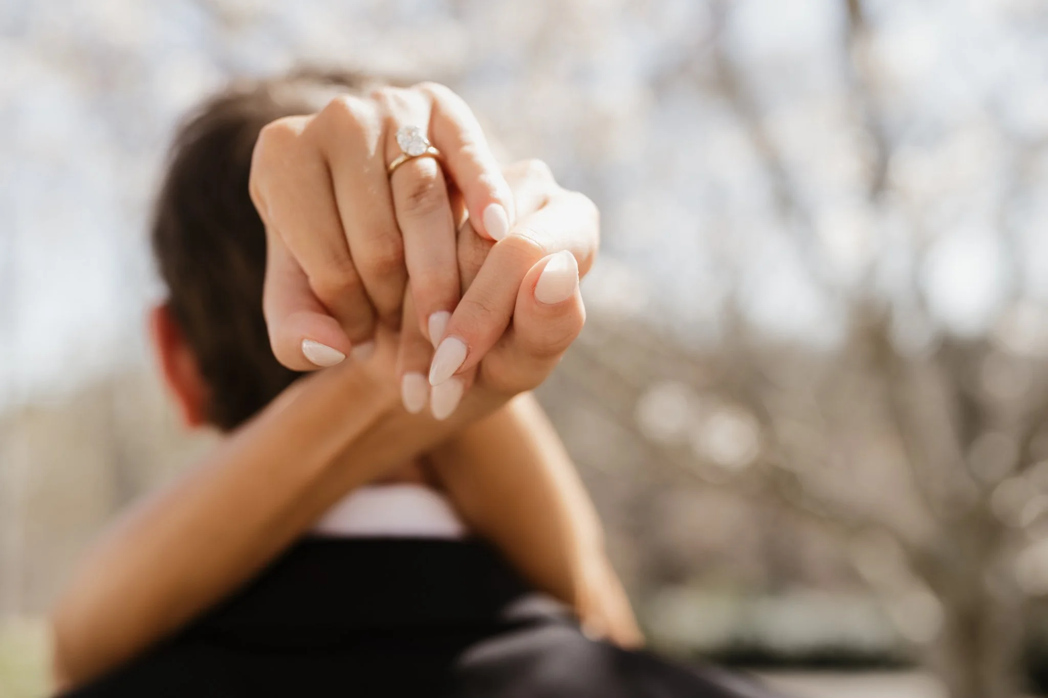 Close-up of a person's hand with a diamond engagement ring, holding another person's hand in Memphis, TN. 